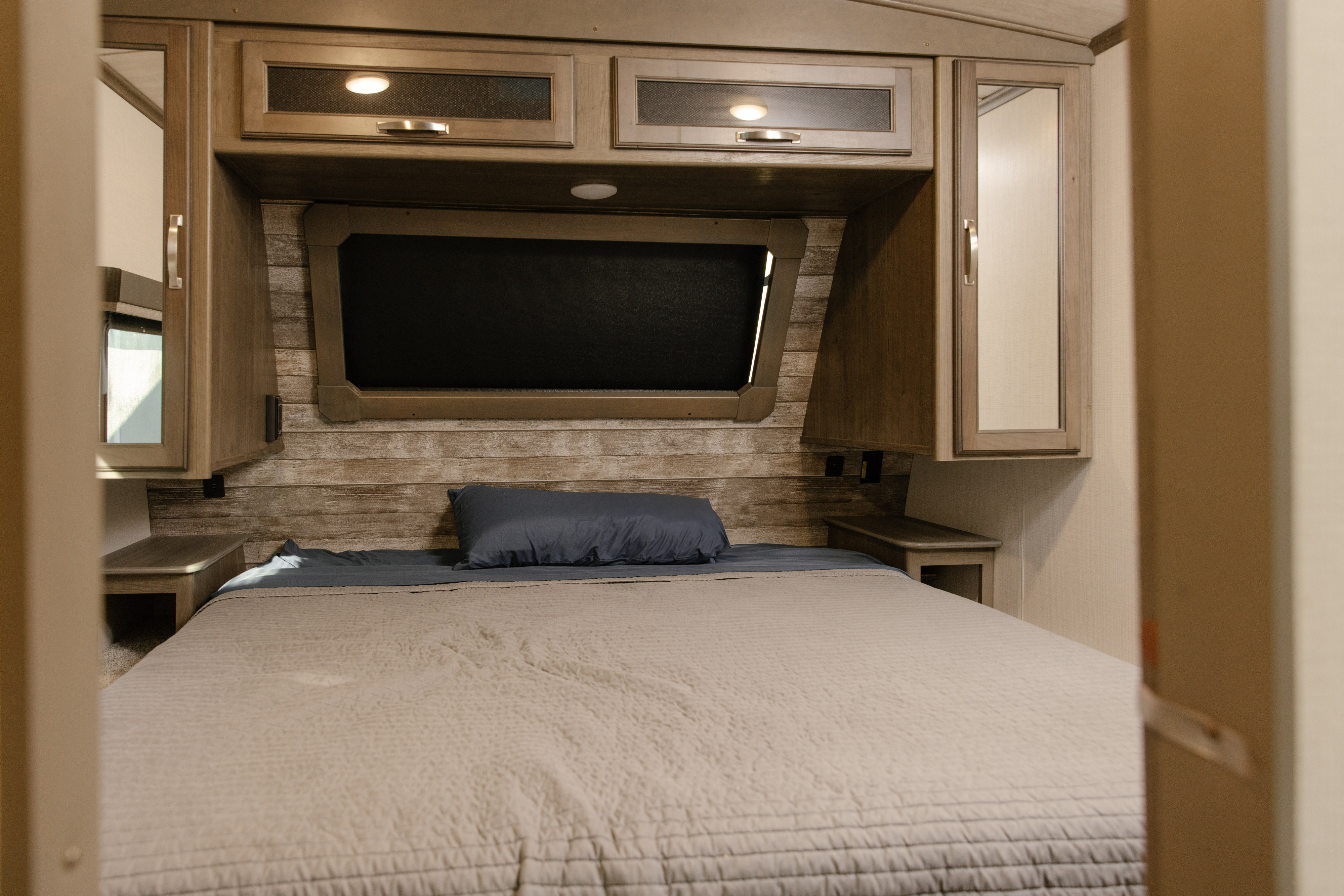 A cozy RV rental bedroom featuring a full-size bed, stylish wood-look headboard, and overhead storage cabinets.. Keystone Cougar Half Ton 2023