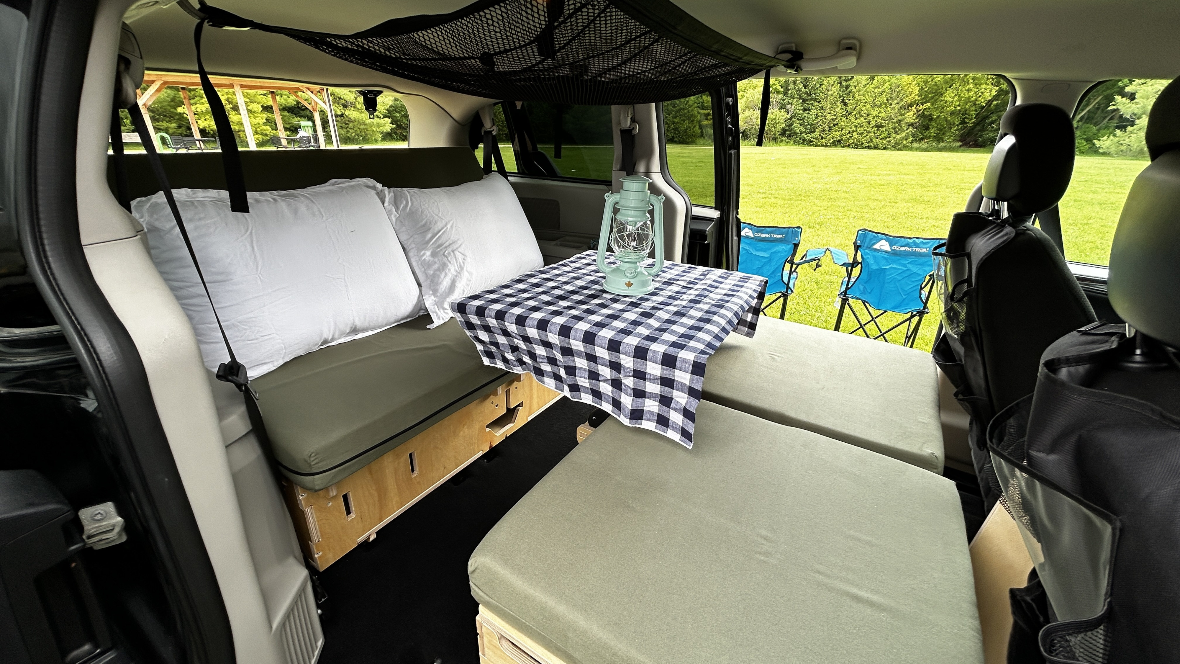 Cozy camper van interior designed for an RV rental. Features a comfy bed, table, storage net, and inviting outdoor view.. Dodge Grand Caravan 2016
