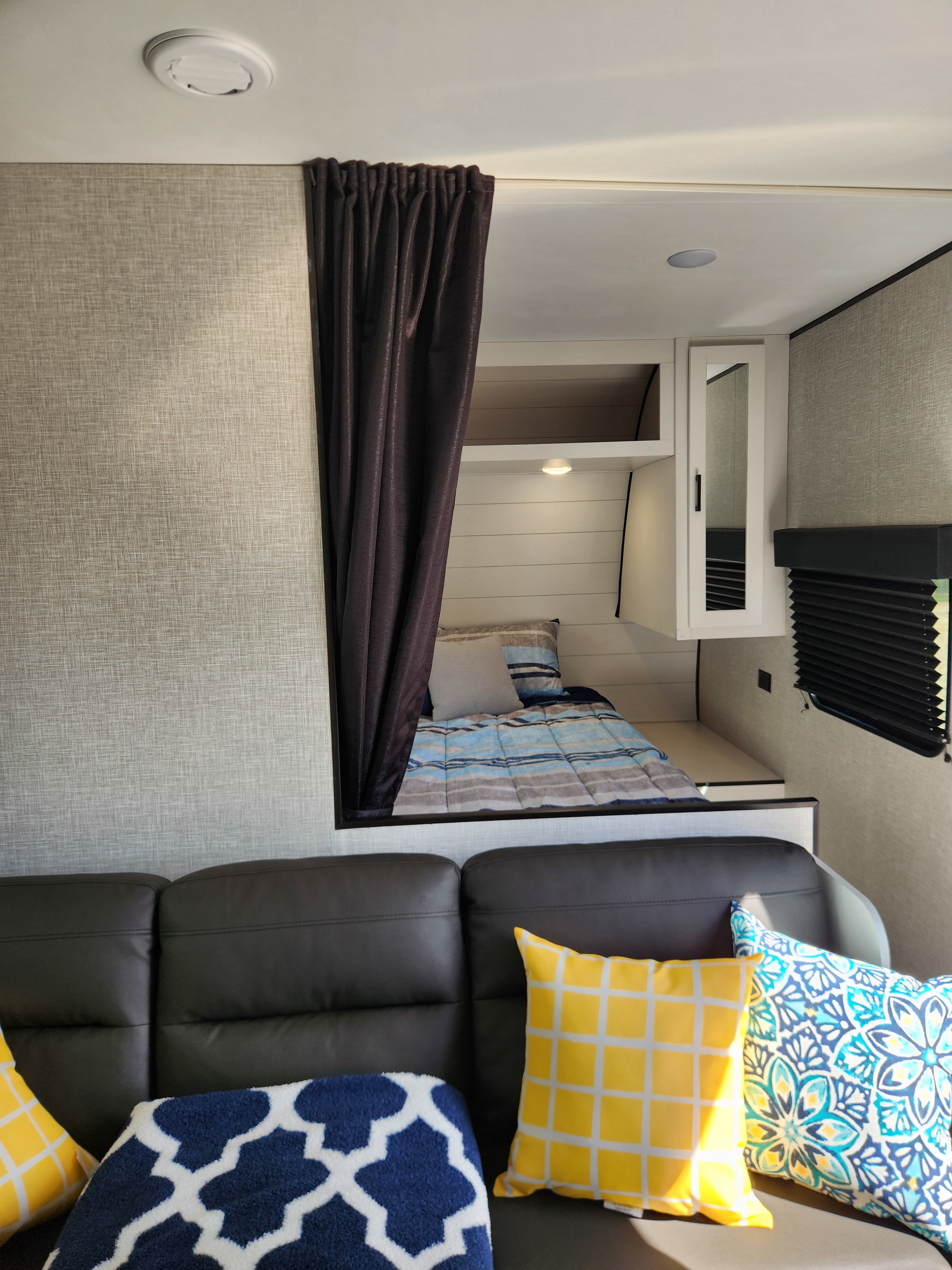 RV rental interior: cozy bunk bed area with a dark curtain, a leather sofa, and colorful throw pillows.. Jayco Jay Flight 2024