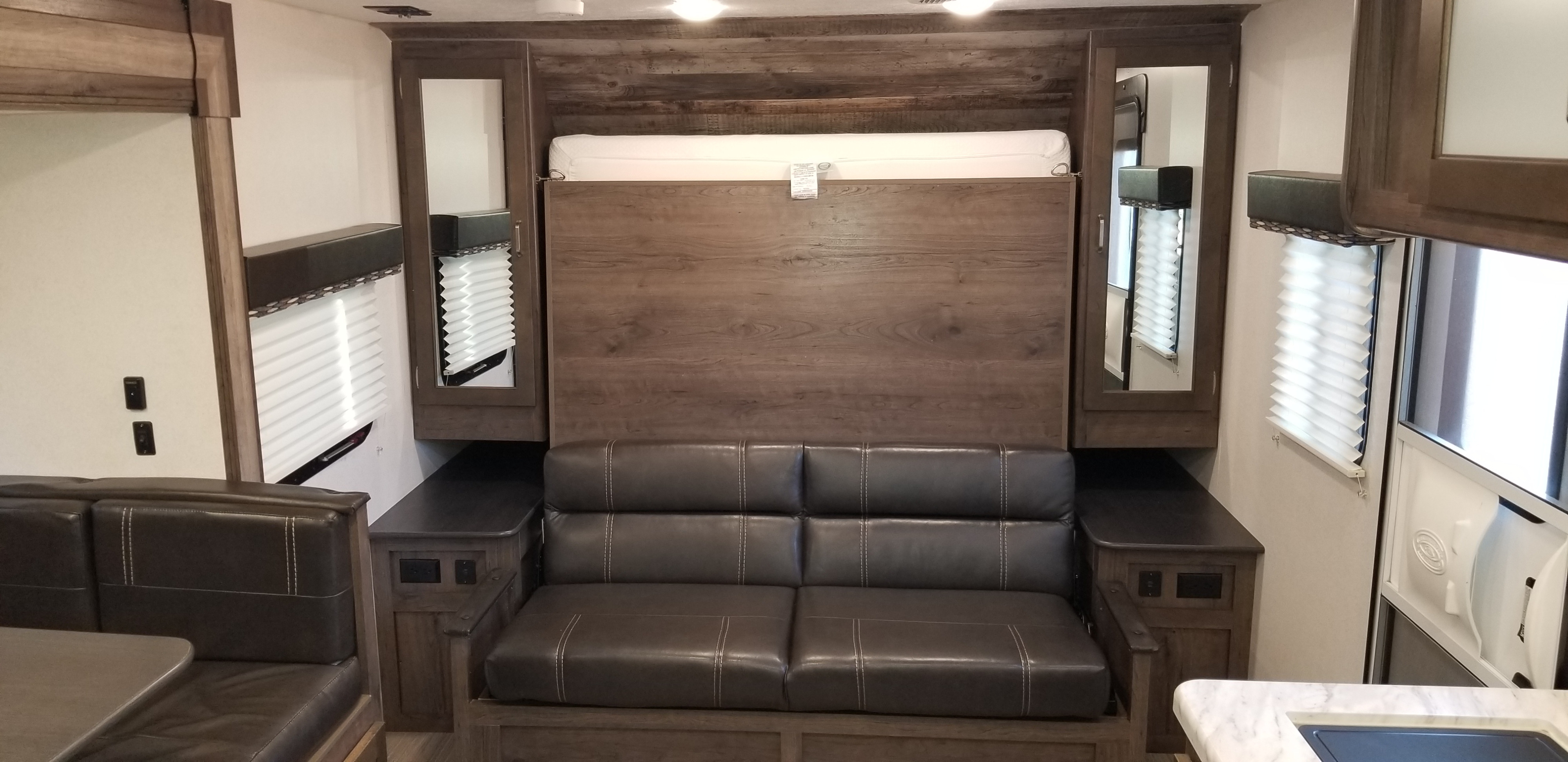 RV rental interior: living area with brown sofa, convertible murphy bed, and wood storage cabinets.. Keystone RV Passport 2019