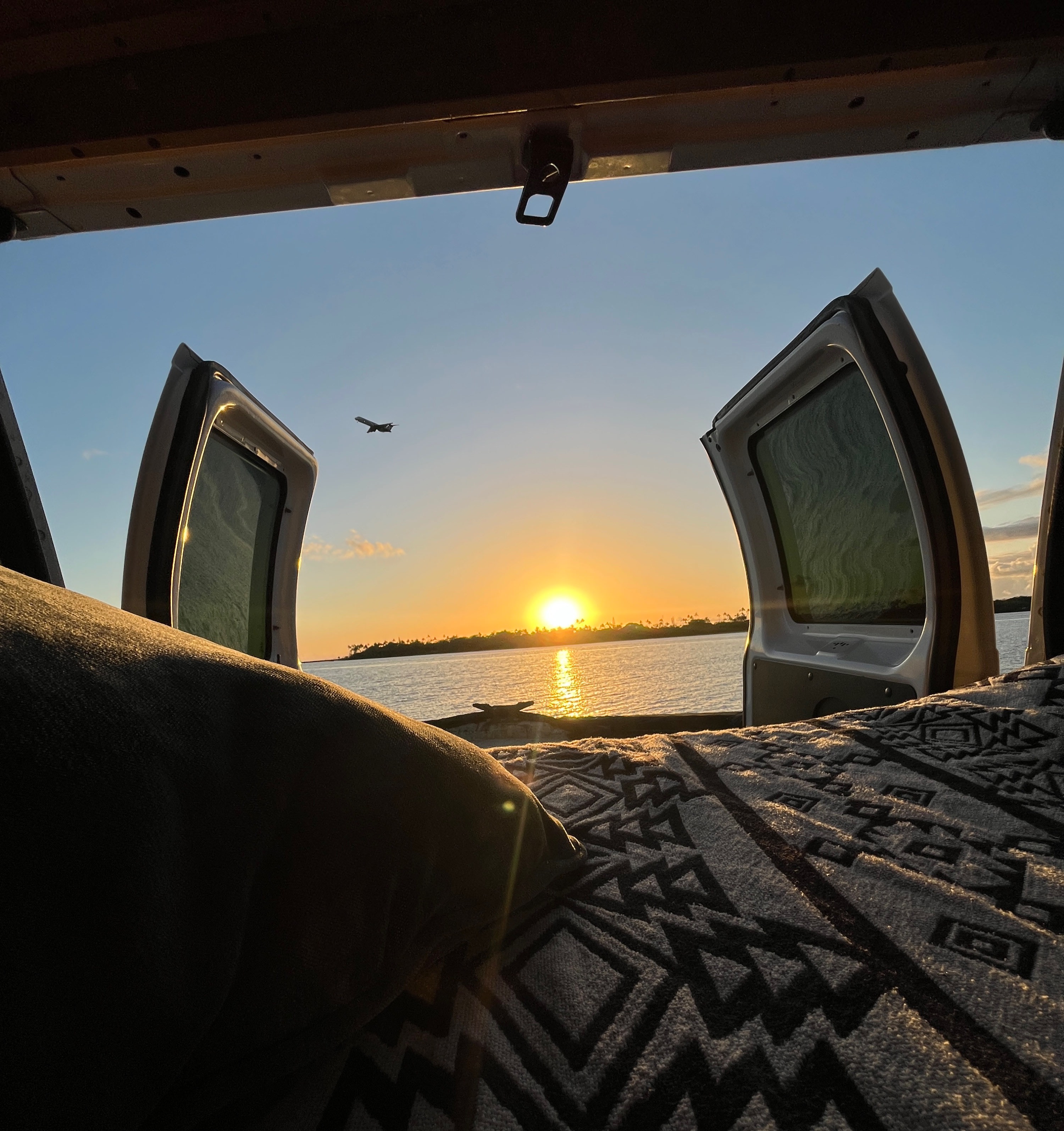 A peaceful RV rental sunset view over the ocean from inside the van, with a plane flying and a cozy bed.. Ford Ford E350 2012