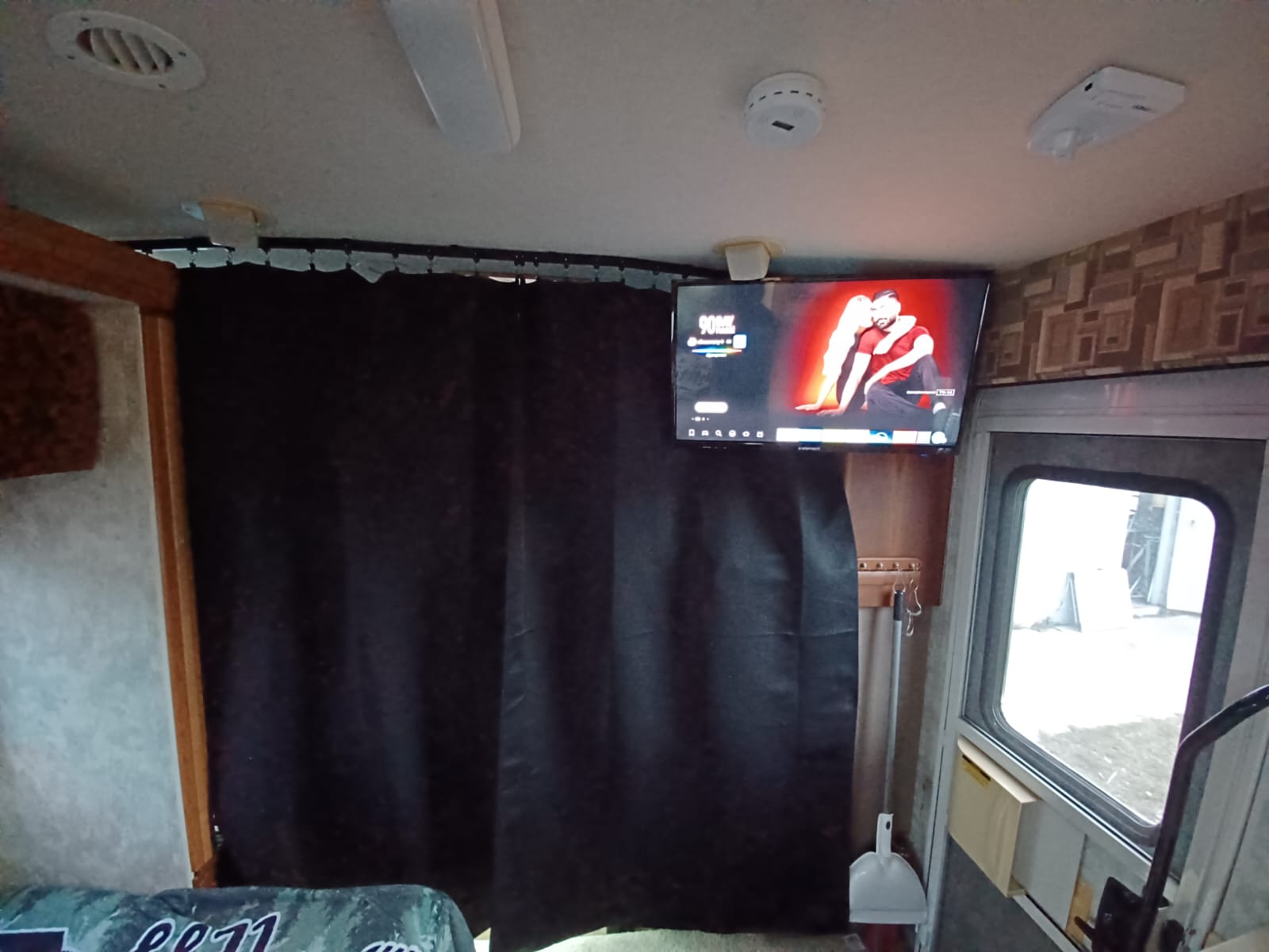 Inside an RV rental: TV displaying a video, ceiling fixtures, and a black privacy curtain dividing the space.. Winnebago Outlook 2007