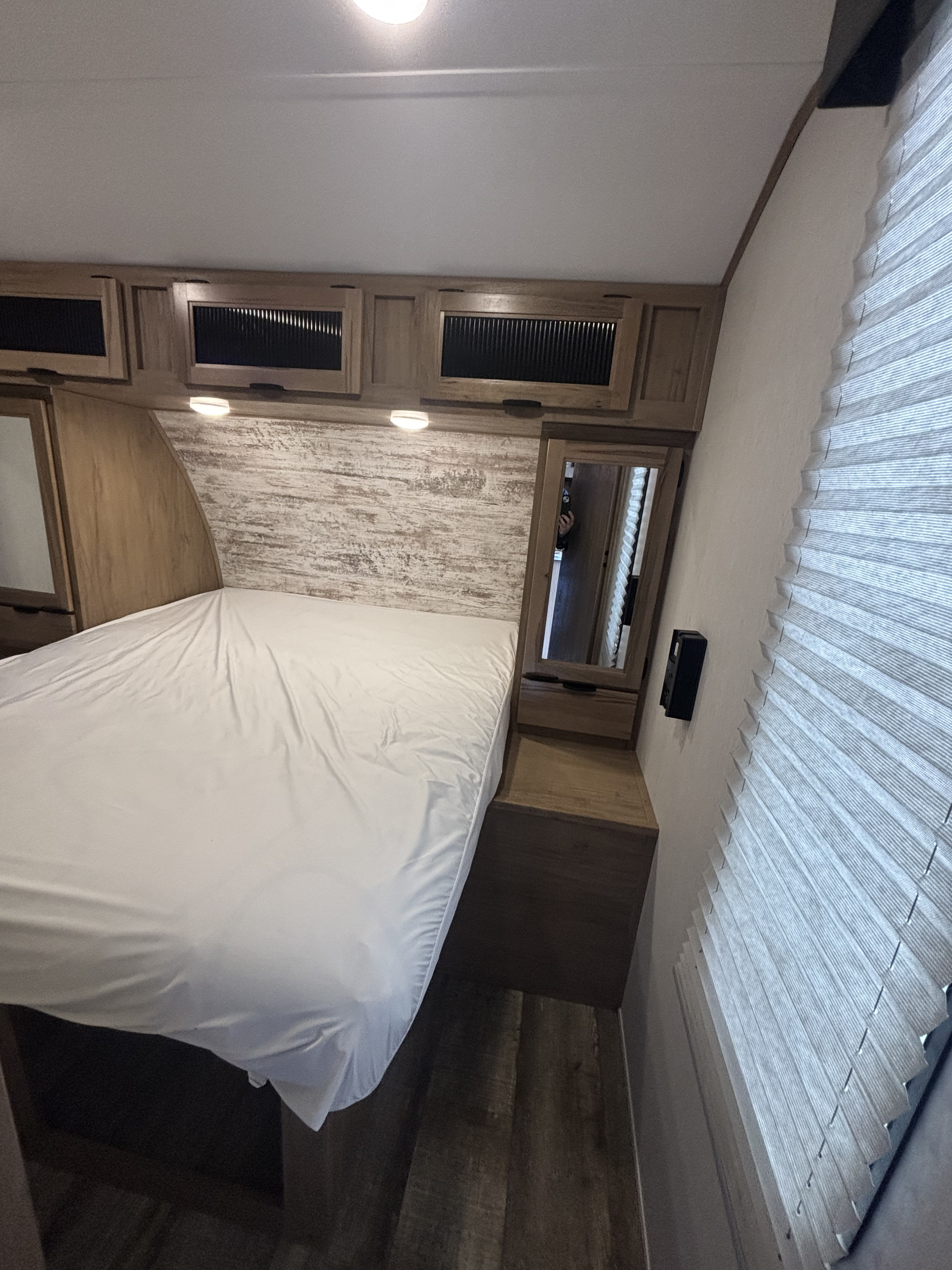 Spacious RV rental bedroom featuring a white-sheeted bed, overhead storage cabinets, and a mirrored nightstand.. Forest River alpha wolf 2023