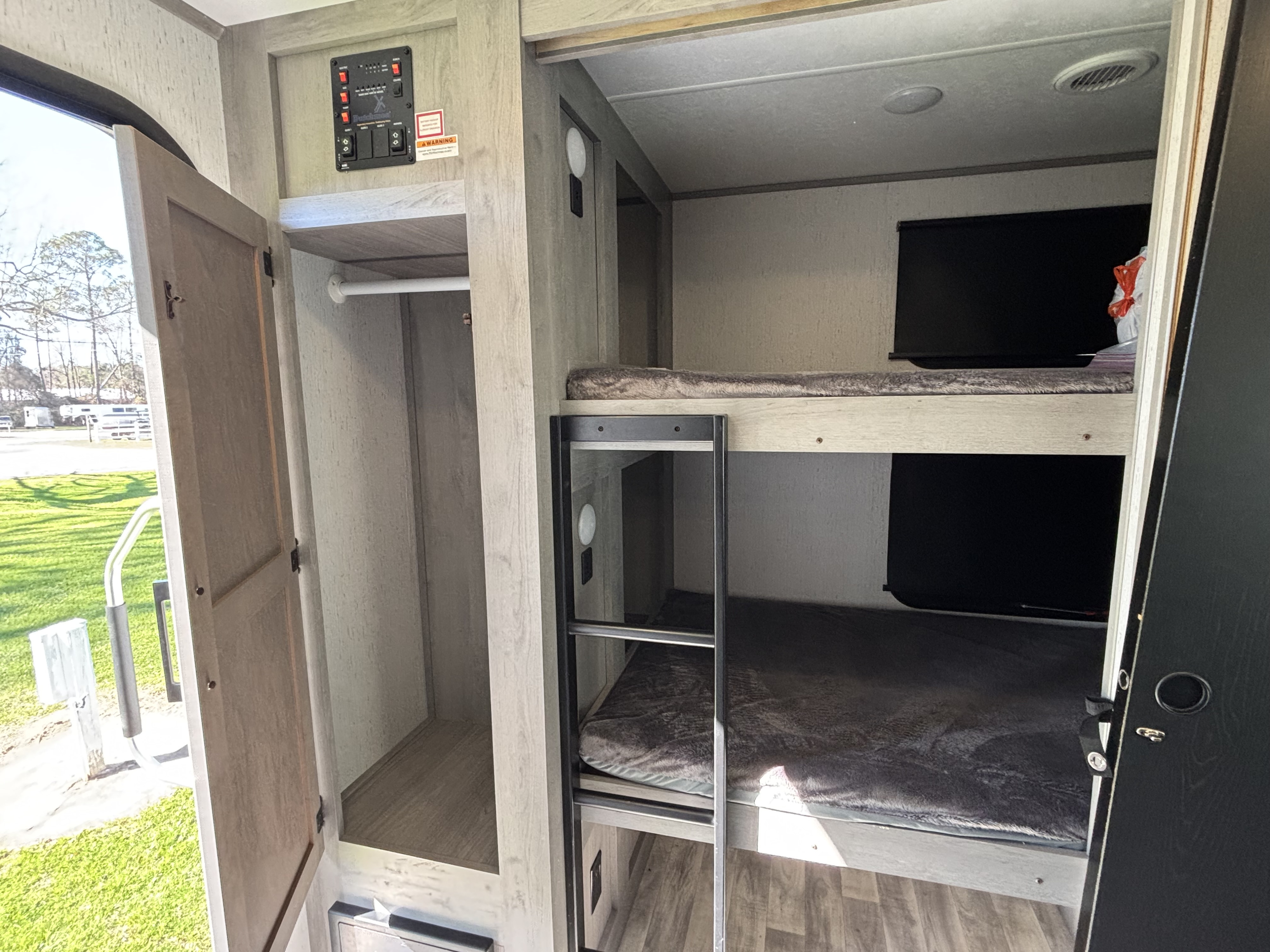 Interior of an RV rental featuring bunk beds, an open storage closet, and a control panel. An outdoor view is visible through the door.. Keystone Kodiak 2022