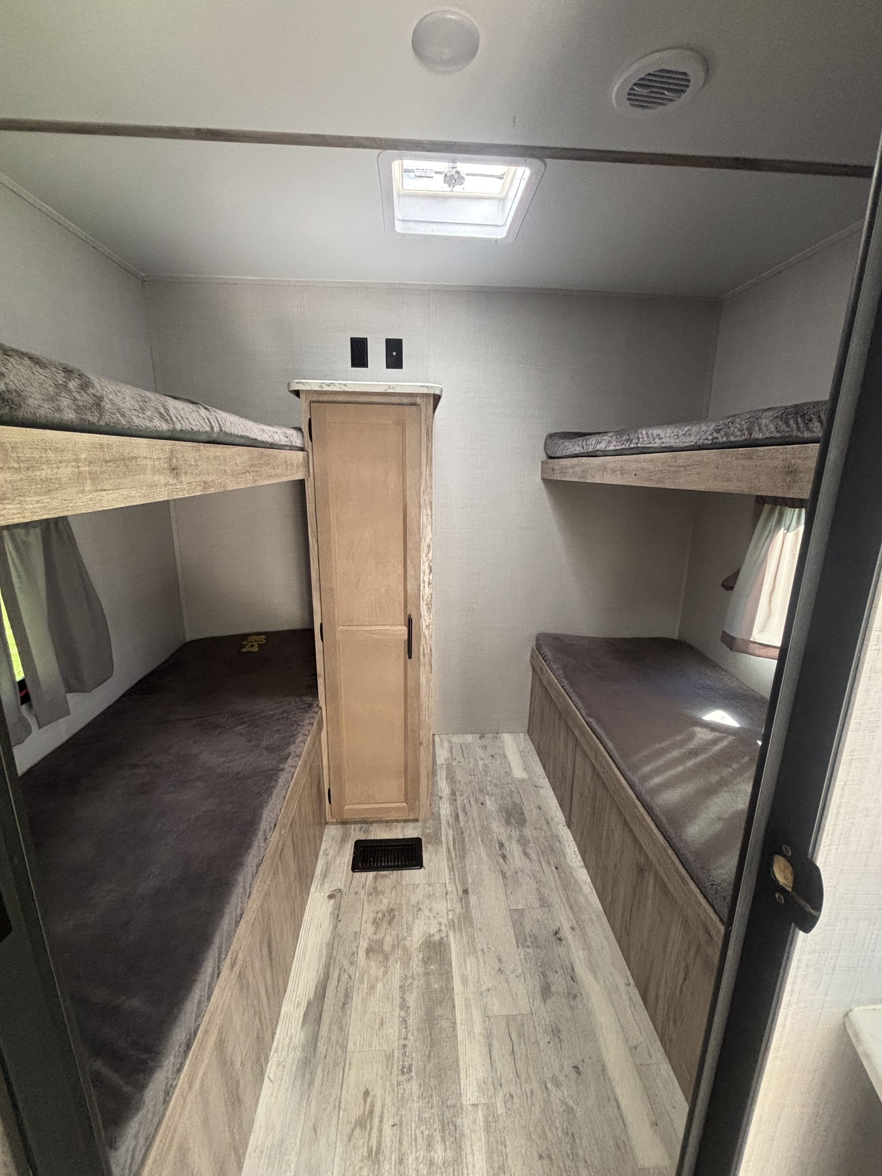 RV rental interior: A cozy bunk room with two sets of beds, a central cabinet, and wood-look flooring, perfect for sleeping.. Gulf Stream Innsbruck 2023