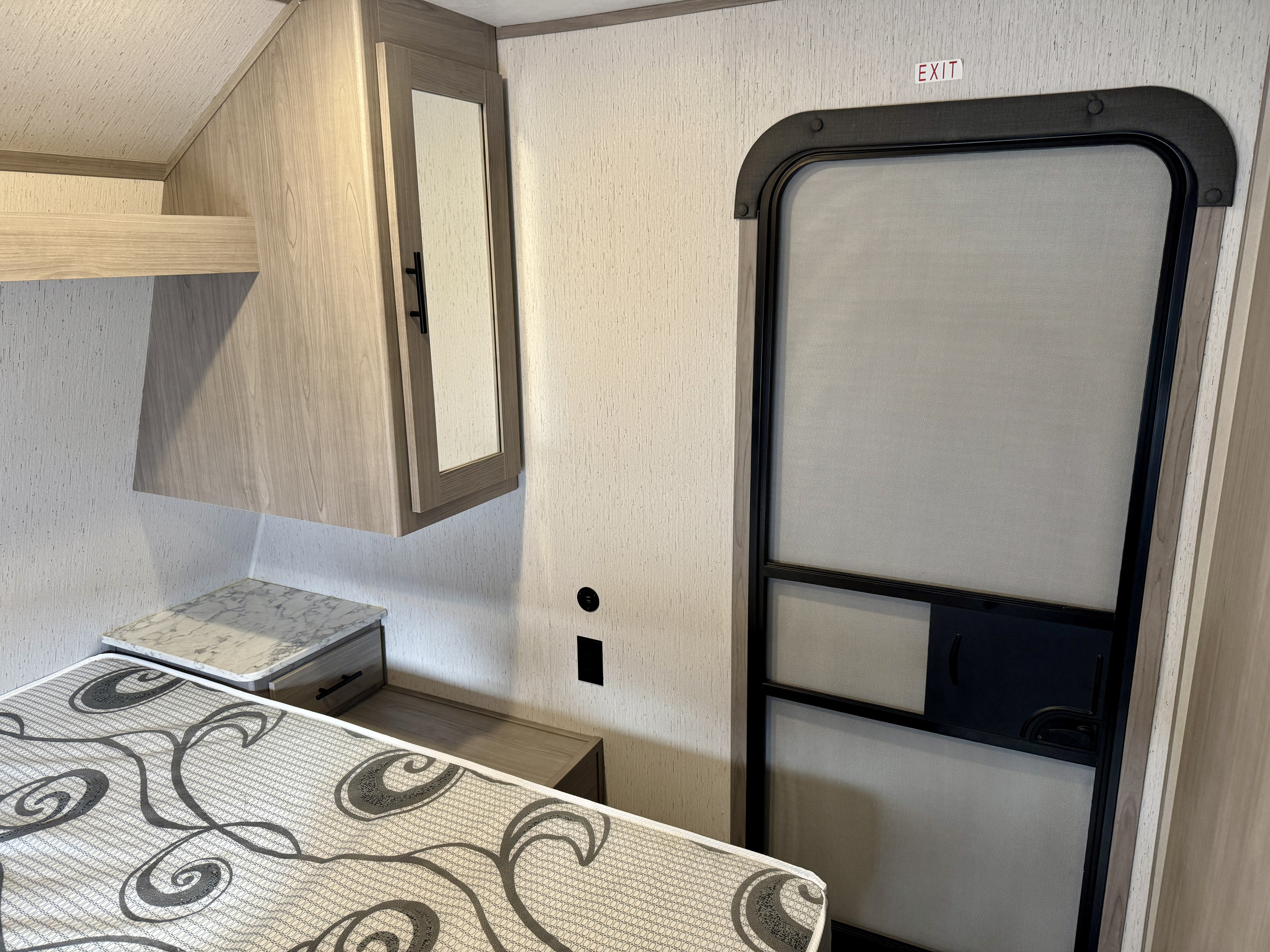 RV rental interior featuring a bed, nightstand, cabinet, and an exit screen door with an "EXIT" sign.. Coleman Lantern 2022