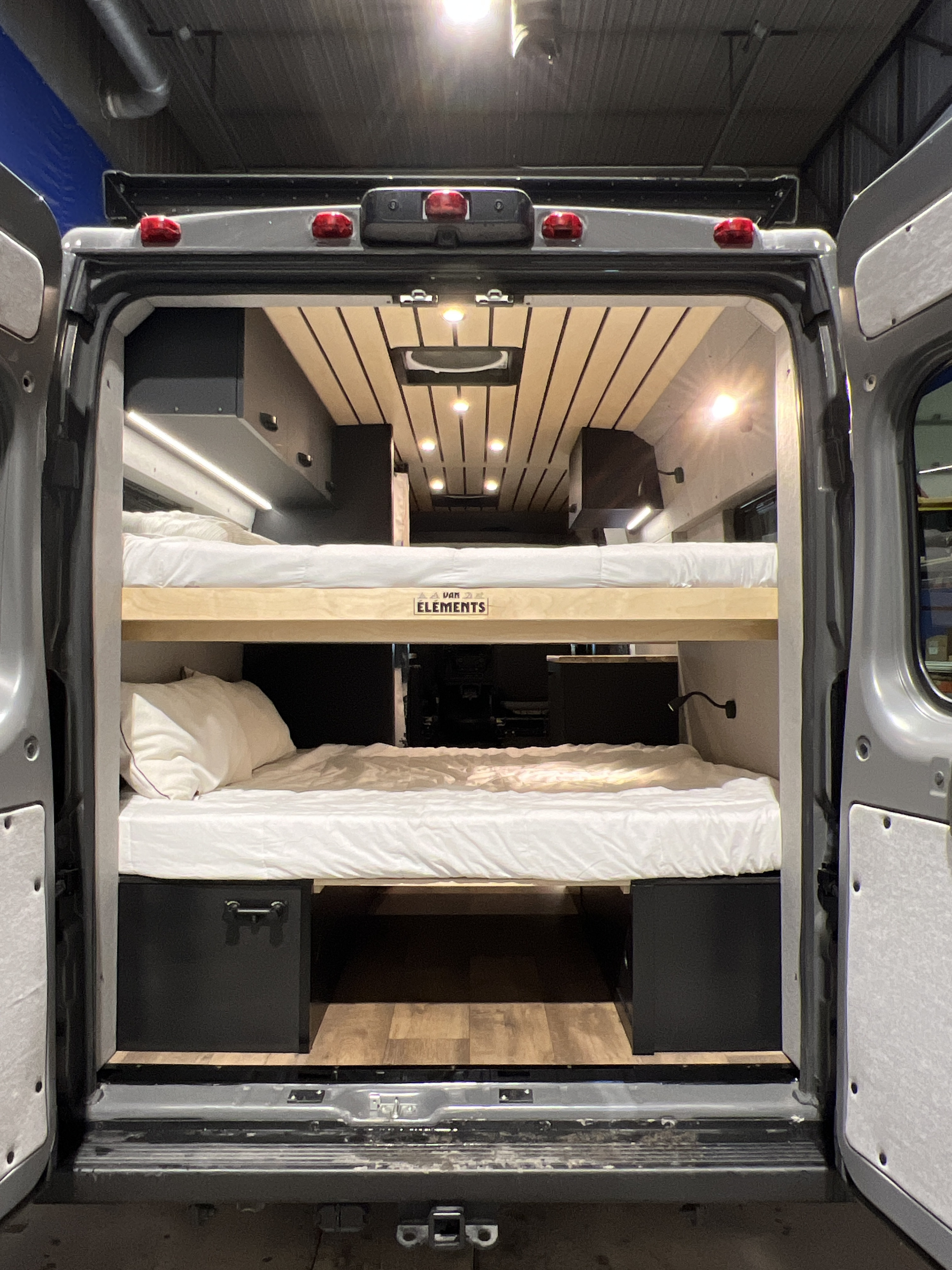 Inside a modern rv rental camper van: two cozy bunk beds with clean white bedding. Bright interior lighting & wood accents.. Dodge Sportsman 2022