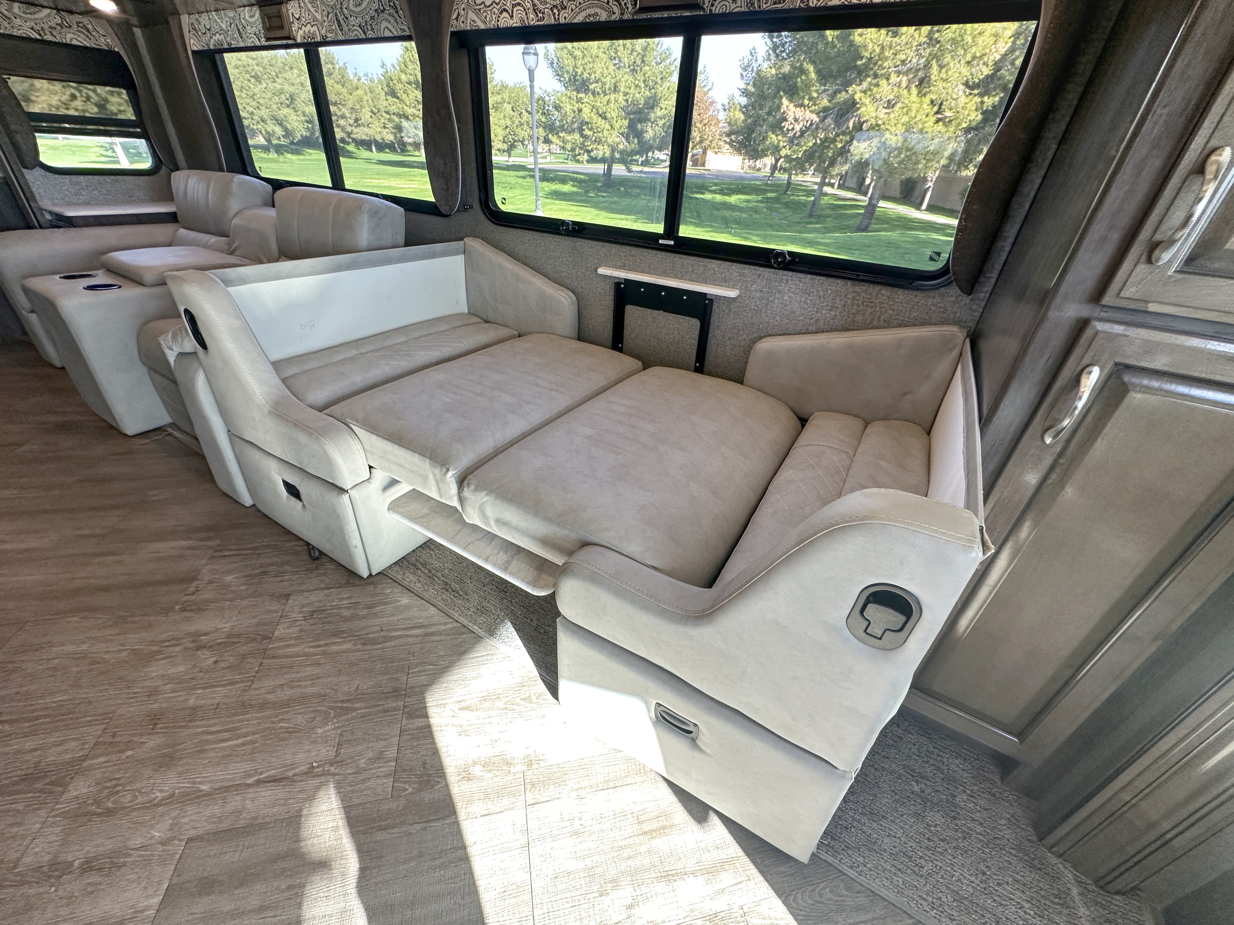 RV rental interior features a versatile light-beige sofa that extends into a bed, with views of green trees outside.. Fleetwood Bounder 2018