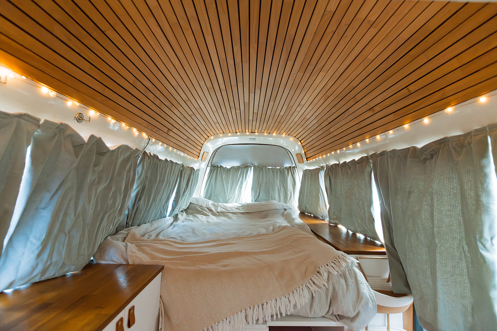 Relaxing RV rental interior: wooden slatted ceiling, fairy lights, and a plush bed, perfect for your next road trip.. Nissan Caravan 2010