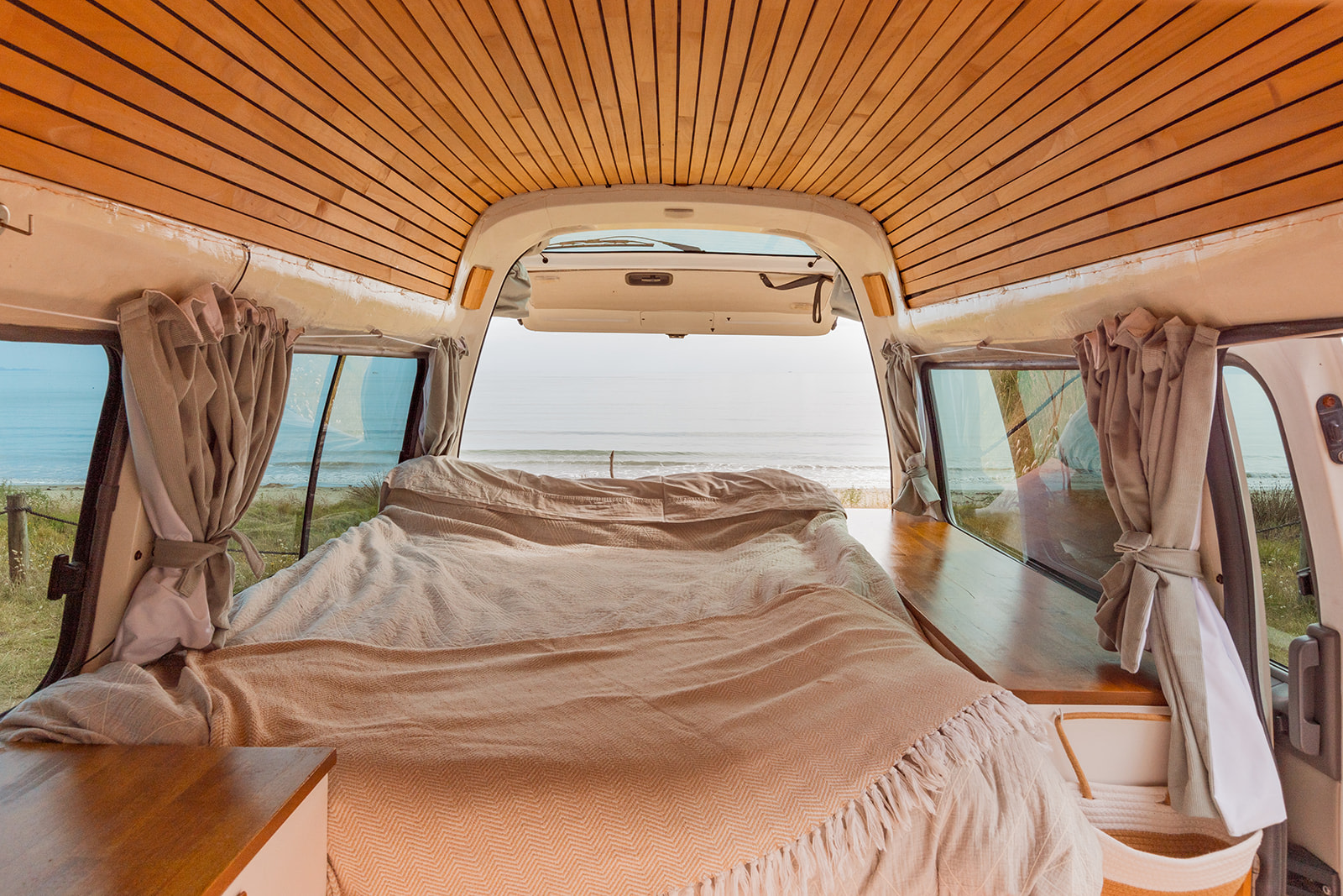 Experience serene travel in this cozy RV rental's bedroom, offering stunning ocean views from the back of the van.. Nissan Caravan 2010