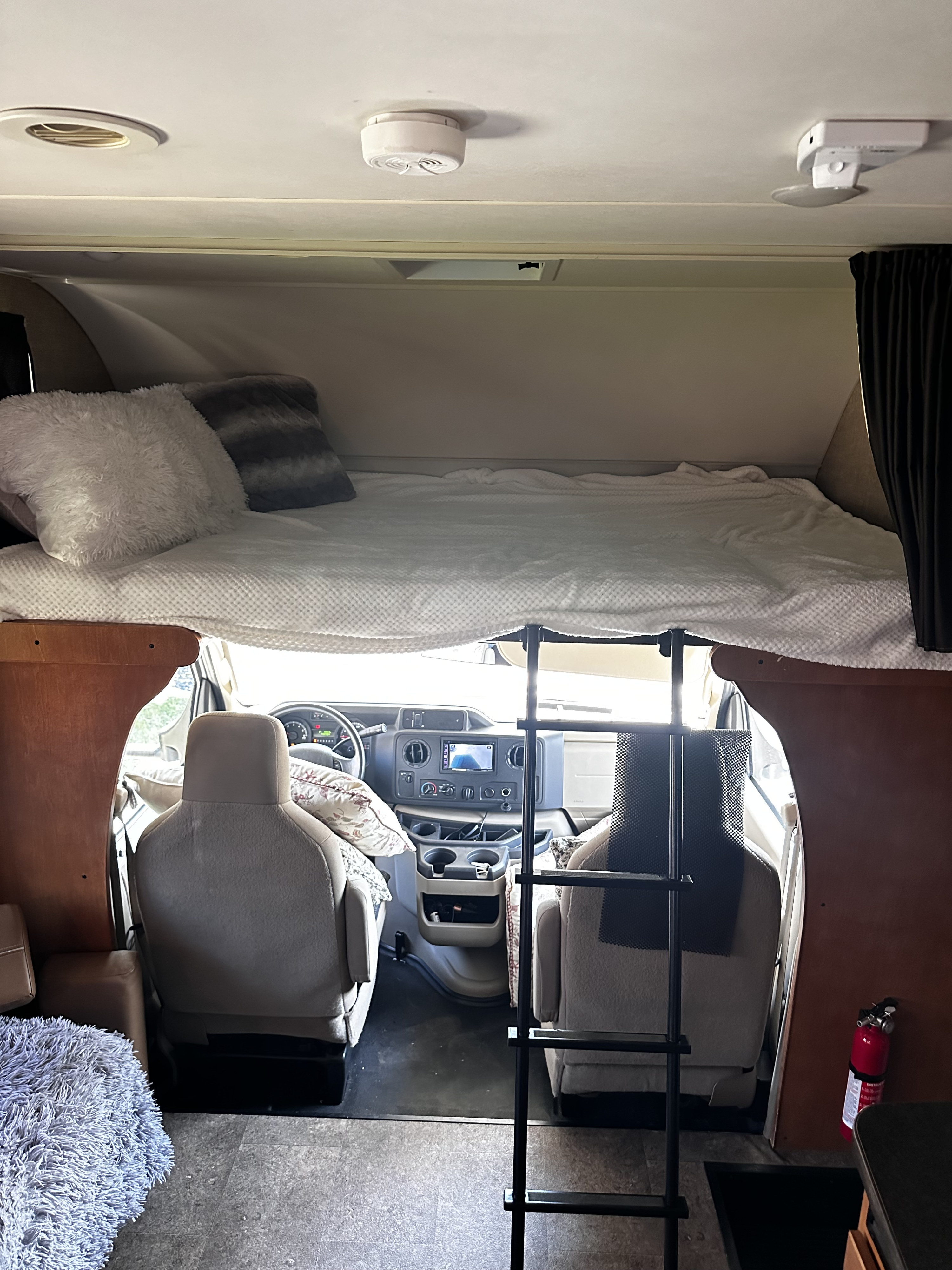 Inside this **rv rental**, a comfy over-cab bunk bed is seen with a ladder leading to the driver's cockpit below.. Winnebago Minnie Winnie 2020