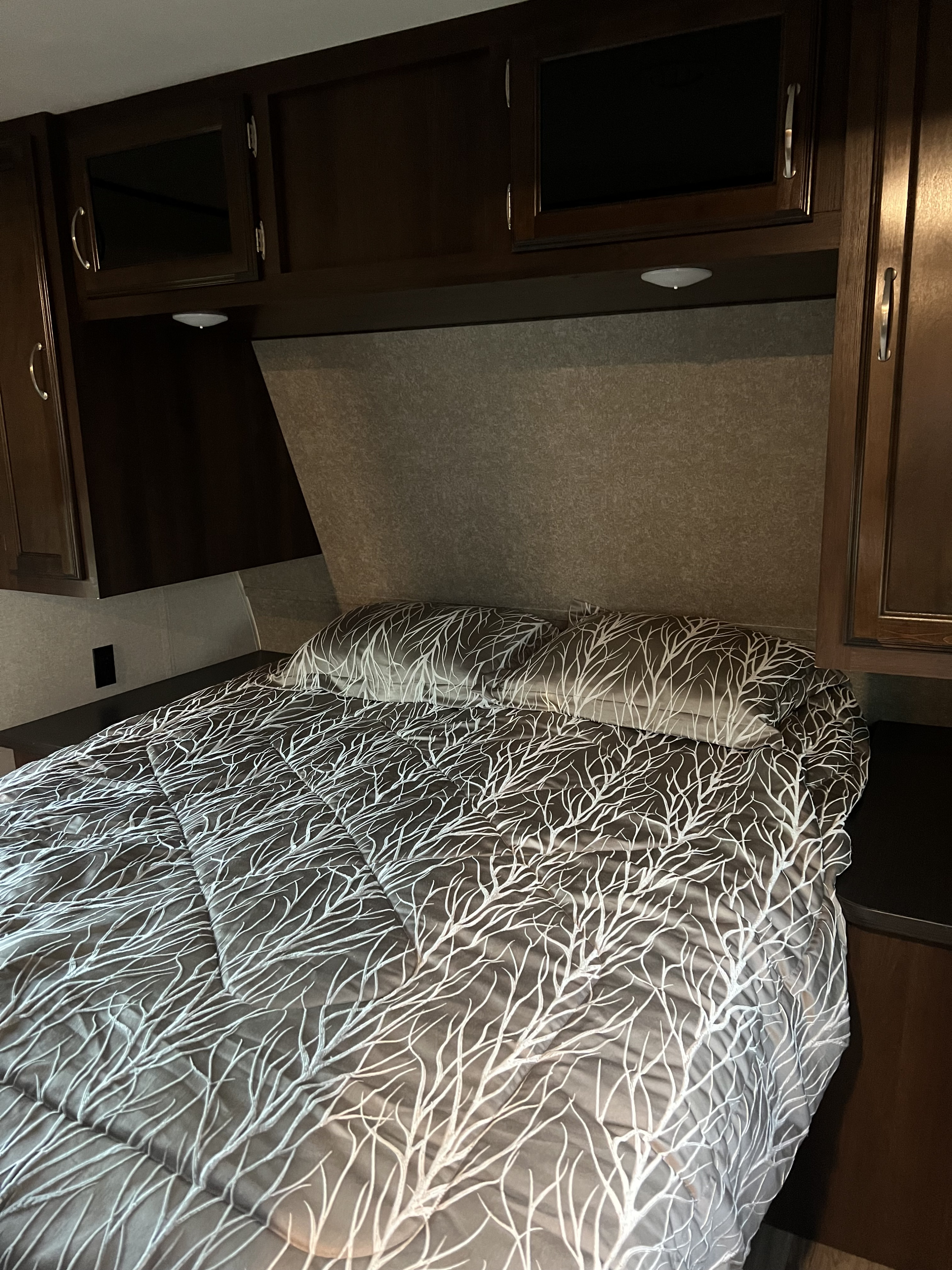 Cozy RV rental bedroom features dark wood cabinets, modern lighting, and a bed with a unique white branch patterned comforter.. Jayco Jay Flight 2018
