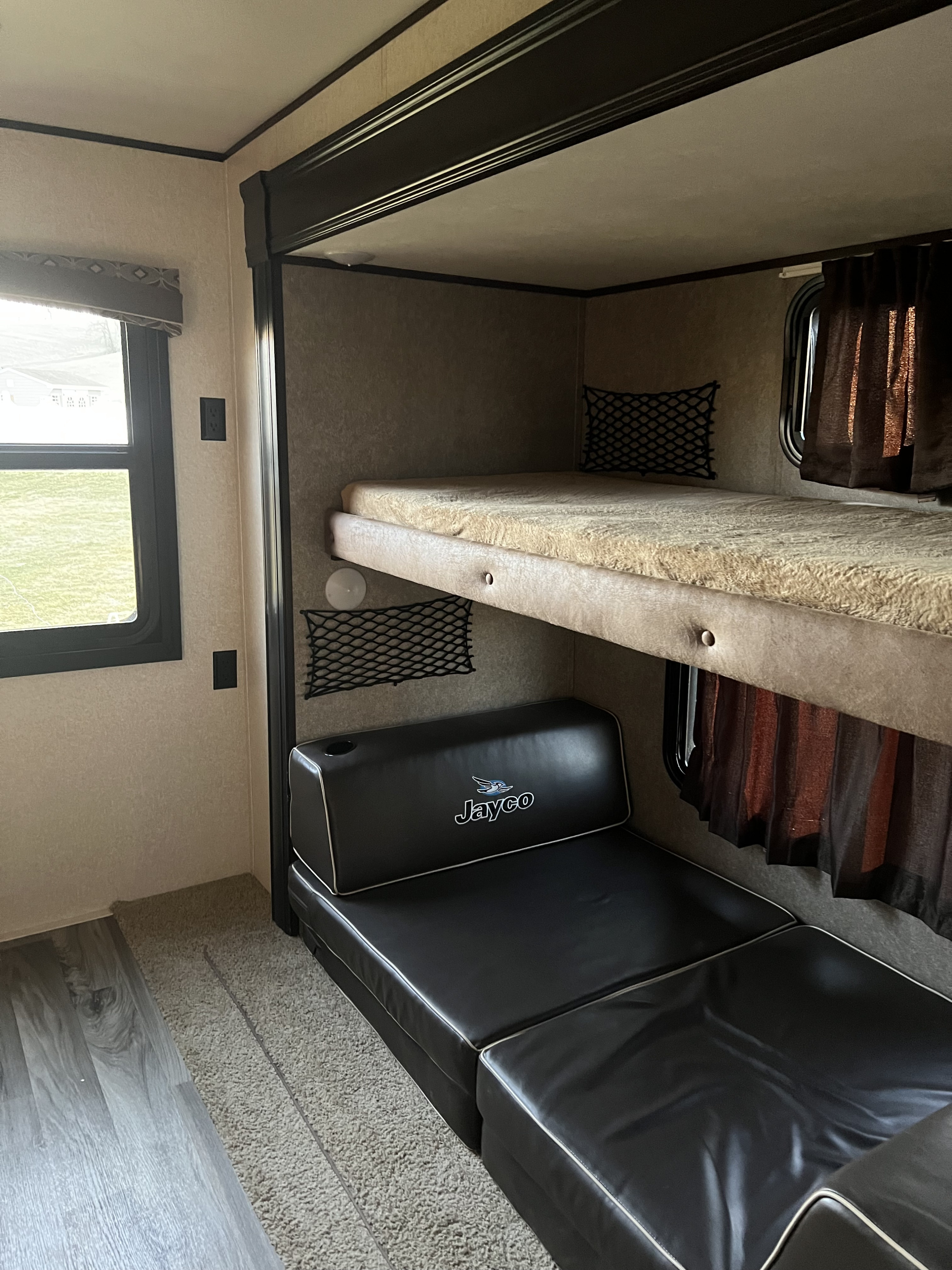 Inside an RV rental: a flexible space featuring comfortable bunk beds and a black convertible sofa below, ideal for resting or lounging.. Jayco Jay Flight 2018