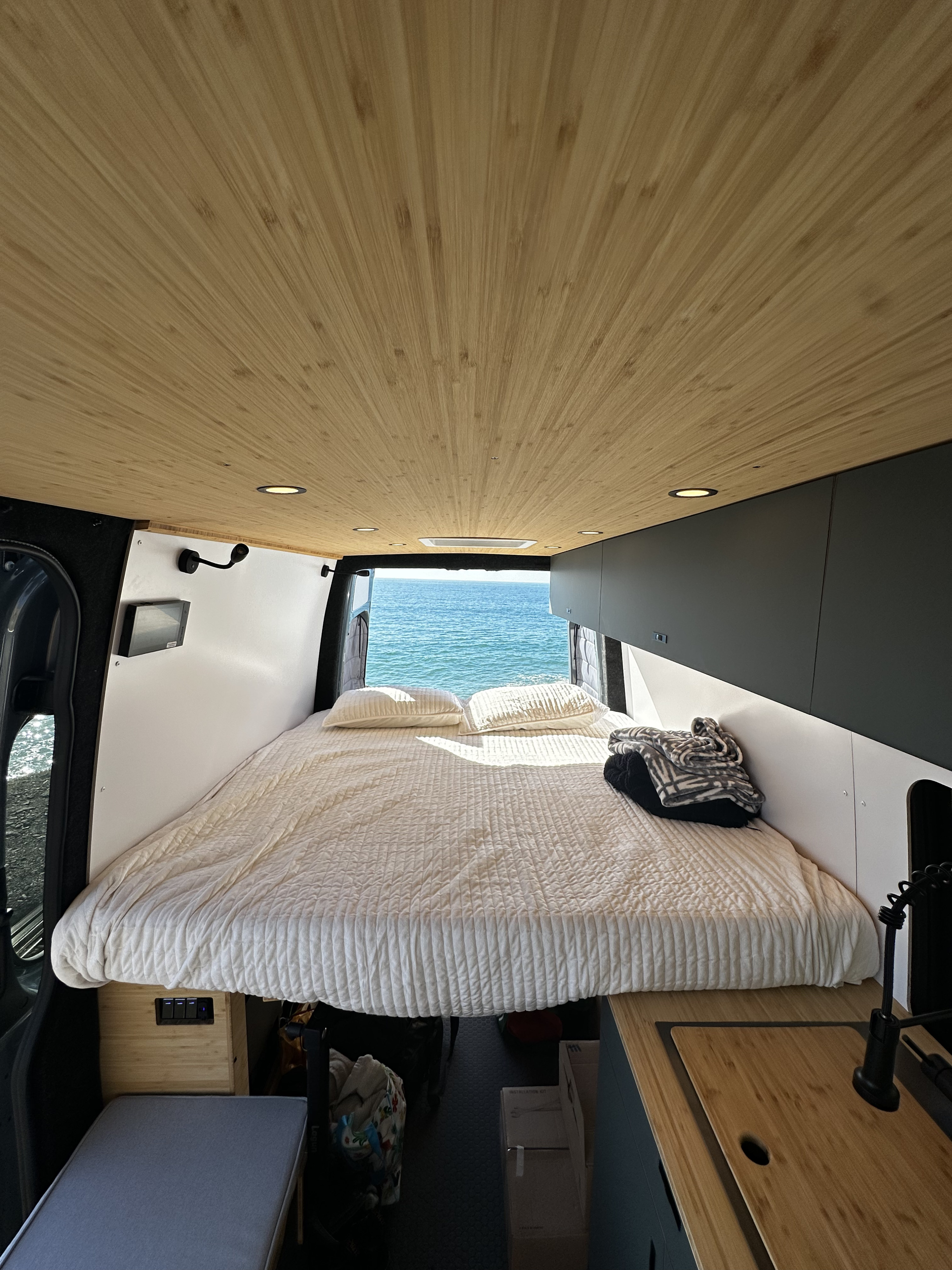 Enjoy this RV rental's cozy interior, featuring a wood-paneled ceiling, comfy bed, and stunning ocean view.. Mercedes-Benz Sprinter 2024