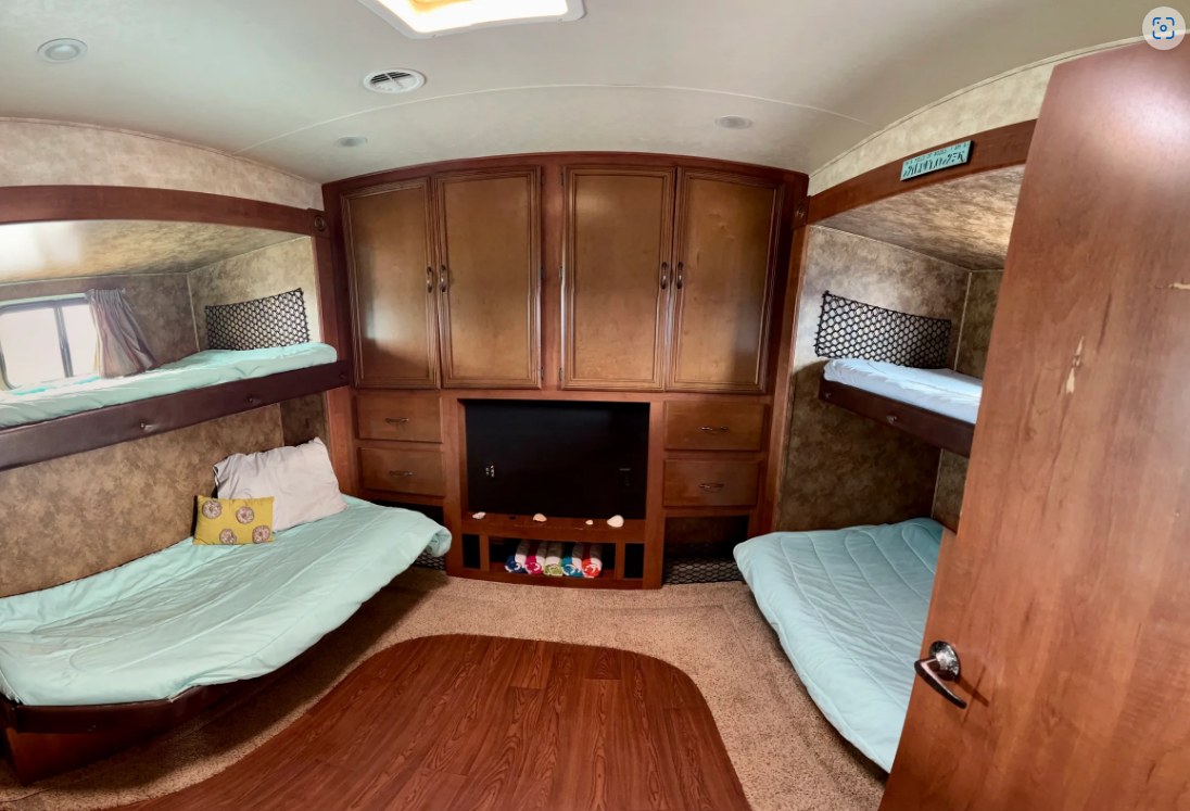 View of an RV rental bunkhouse with four beds, a central TV, and storage, designed for comfortable travel.. Forest River Sandpiper 2012