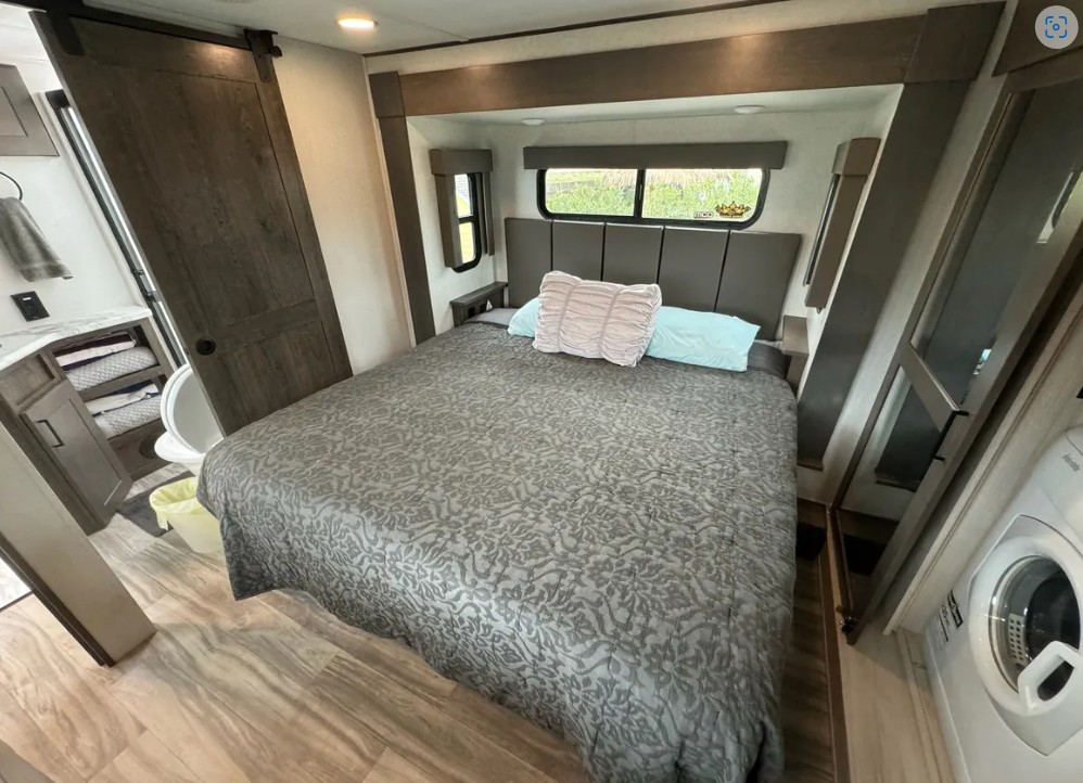 This RV rental bedroom features a comfy bed, barn door to bathroom, windows, and a convenient washer.. Alliance Valor 2022