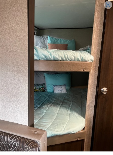 Cozy bunk beds with aqua bedding and decorative pillows provide sleeping space in this RV rental, visible through a narrow doorway.. Keystone Springdale 2018