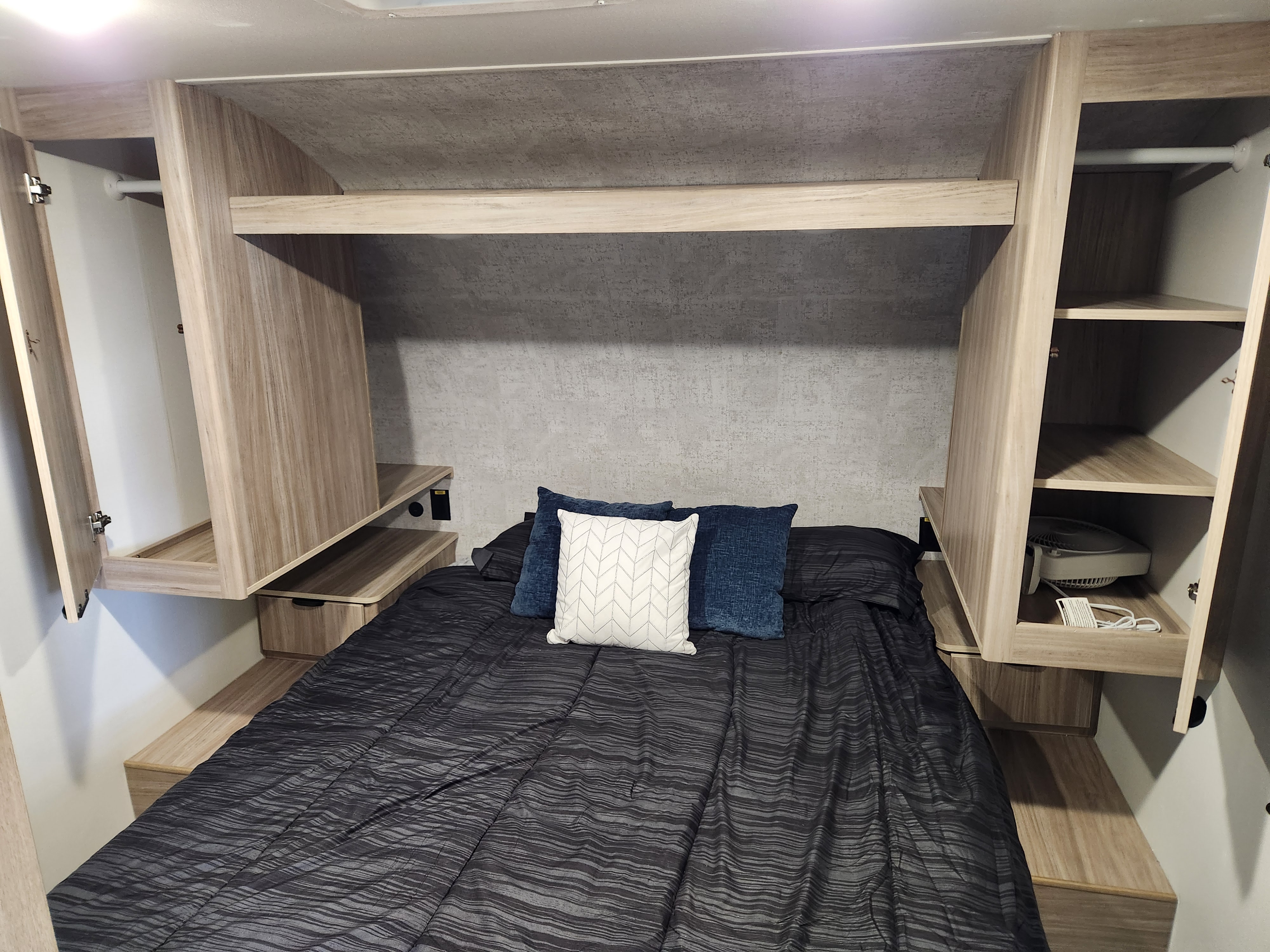 Modern RV rental bedroom with light wood cabinetry, overhead storage, and side closets, providing practical comfort.. Winnebago Access 2024