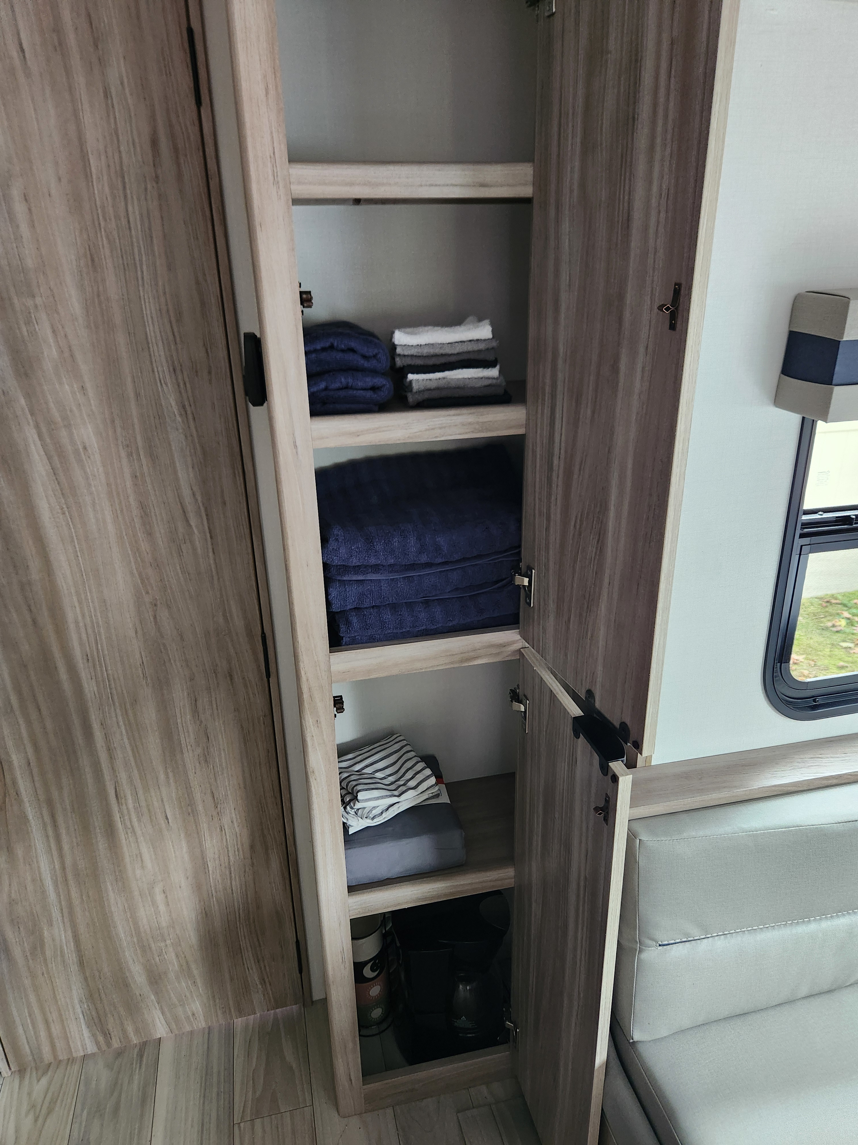 RV rental: Open cabinet storage in an RV interior, neatly stocked with folded blue and gray towels.. Winnebago Access 2024