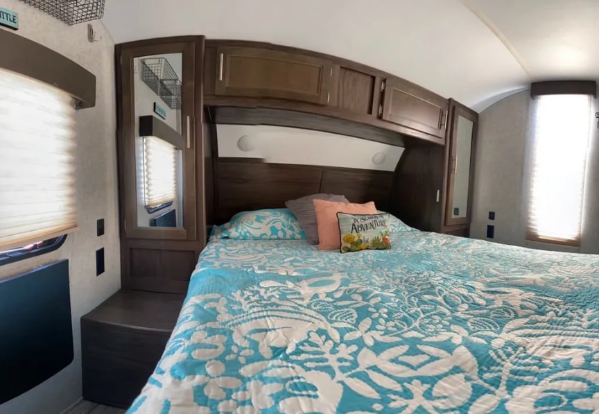 Cozy RV rental bedroom with patterned bedding, overhead storage, and windows, offering comfortable travel accommodations.. Forest River Cherokee 2018