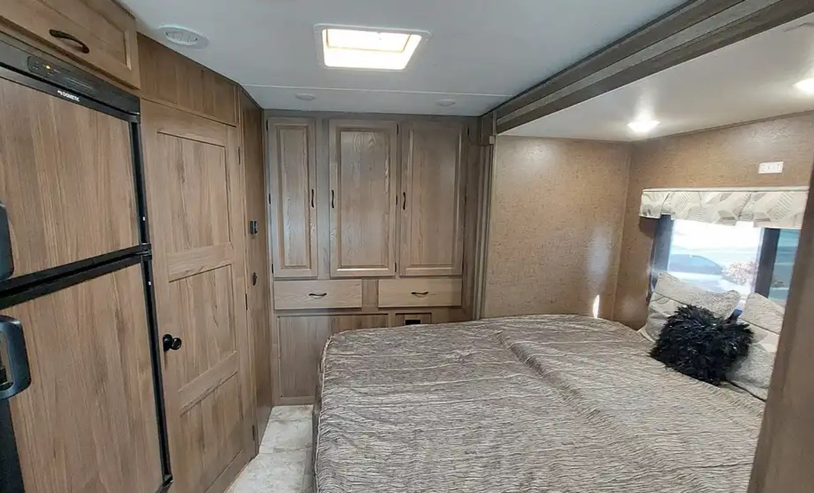 Spacious rv rental interior showing a comfortable bed, built-in wood cabinets for storage, and a Dometic refrigerator.. Forest River Coachmen Prism 2019