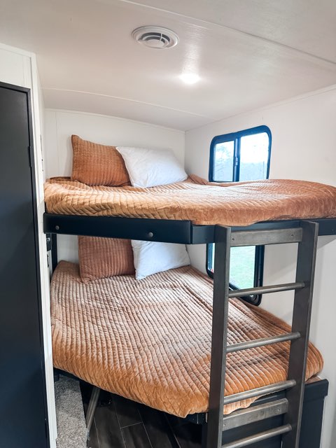 Two bunk beds in an RV rental, with quilted orange bedding and pillows. A ladder is positioned for access.. Keystone RV Passport GT 2022