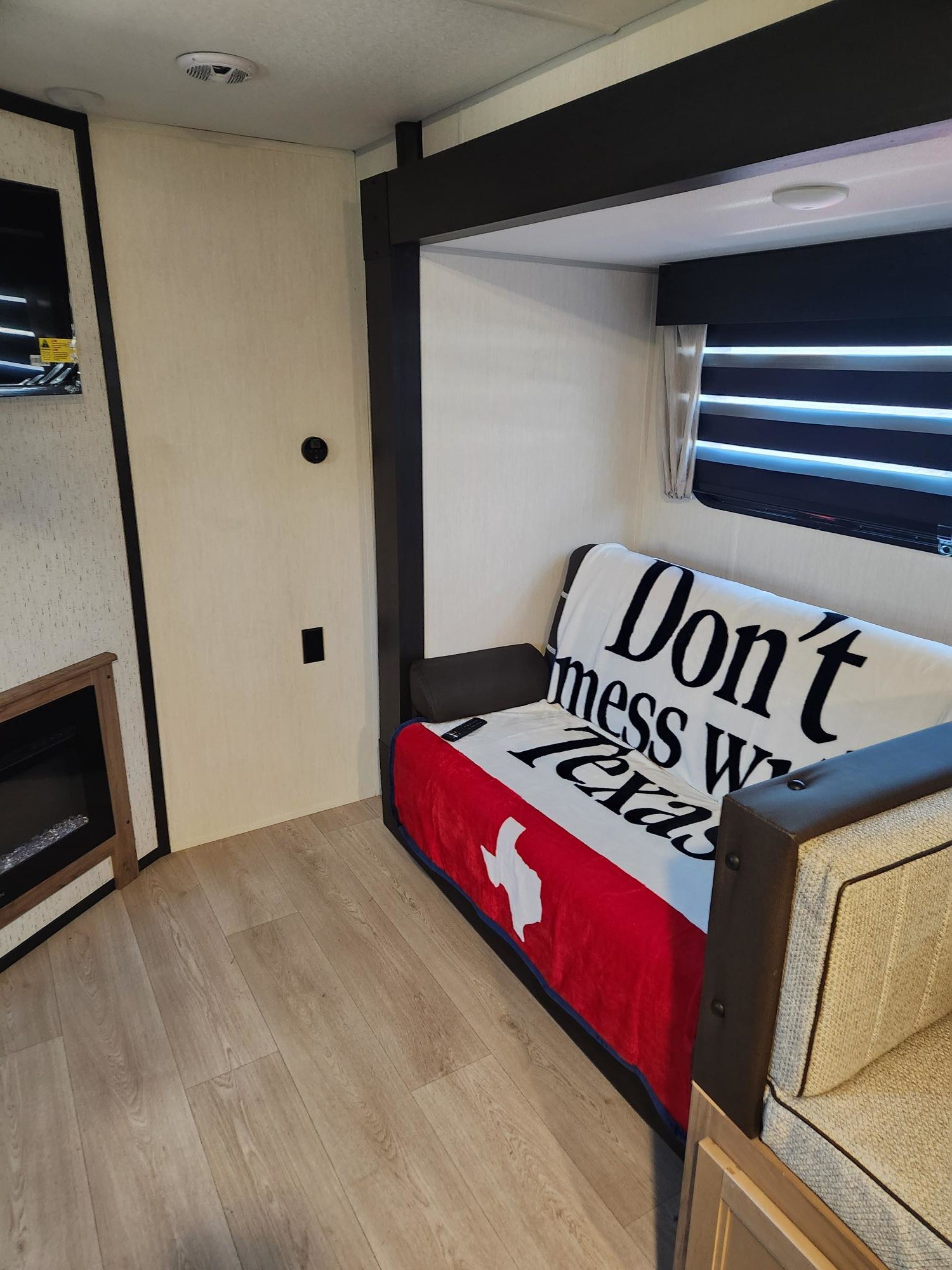 Inside an RV rental: A warm living area with a couch, Texas blanket, TV, electric fireplace, and light wood flooring.. Forest River/ Grey Wolfe Black Label 29NMBL 2025