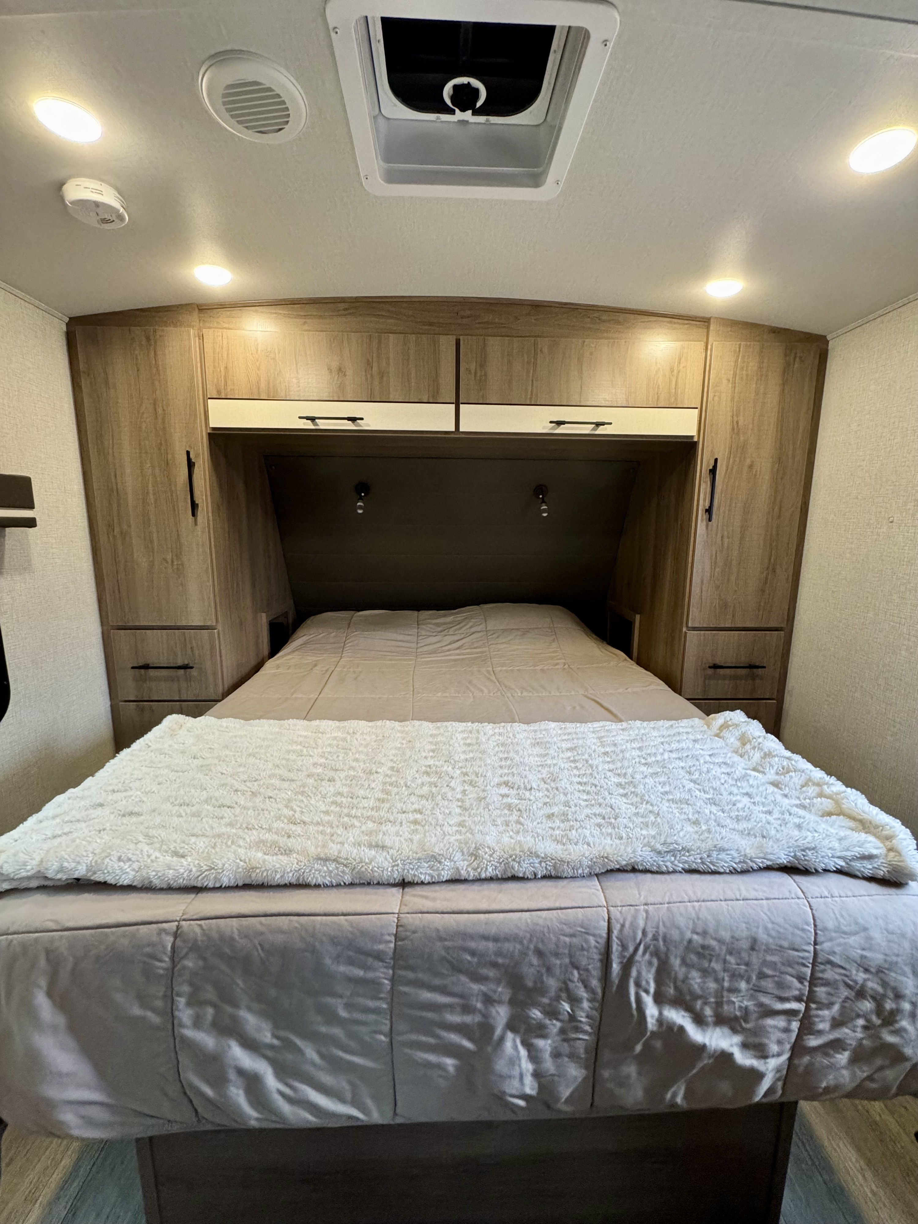 Cozy RV rental bedroom featuring a comfortable bed, overhead cabinets, reading lights, and ceiling vent for a relaxing stay.. Grand Design Imagine 2023