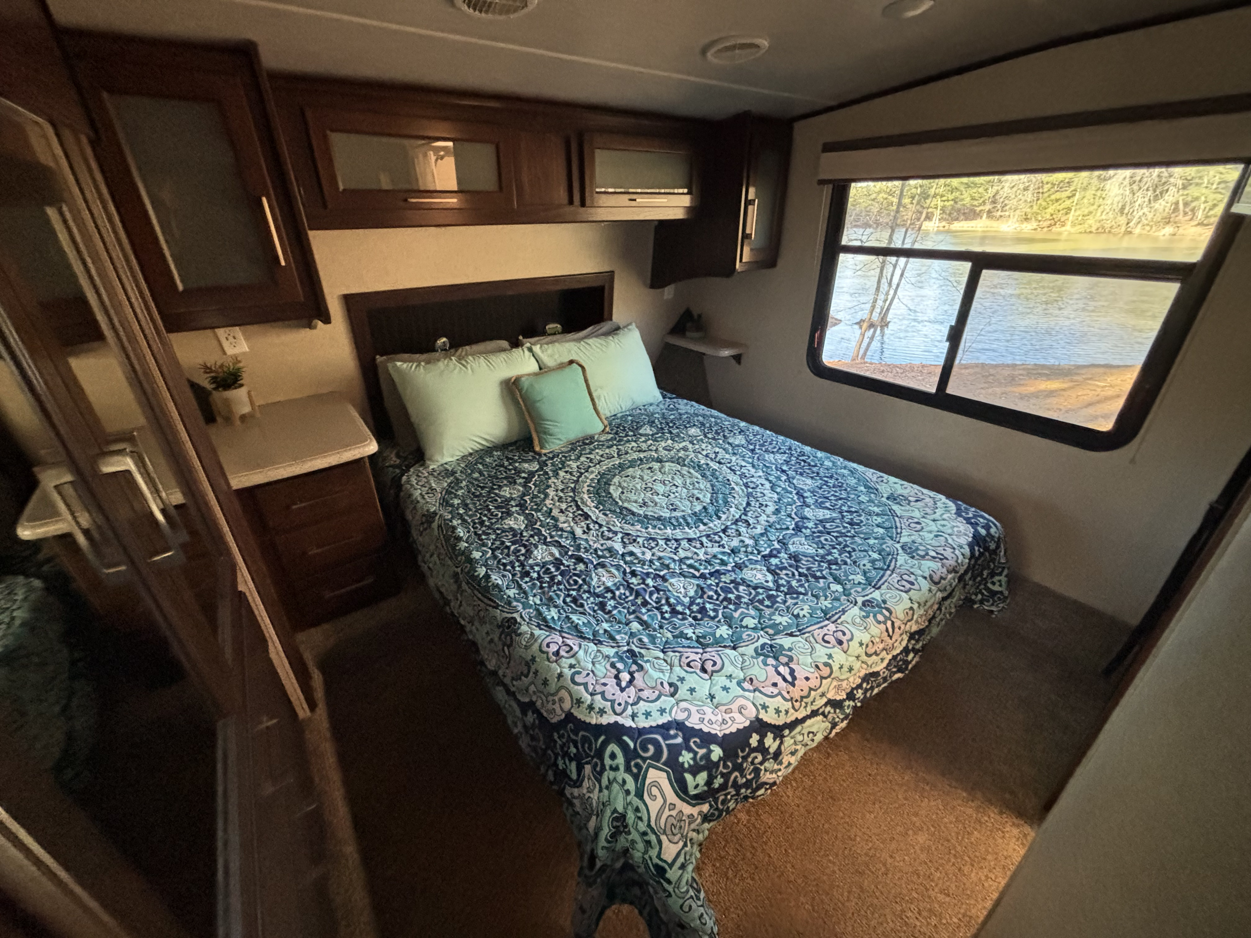 Enjoy a serene lake view from this cozy RV rental bedroom. Features a vibrant blue mandala comforter and ample storage.. Heartland Cyclone 2018