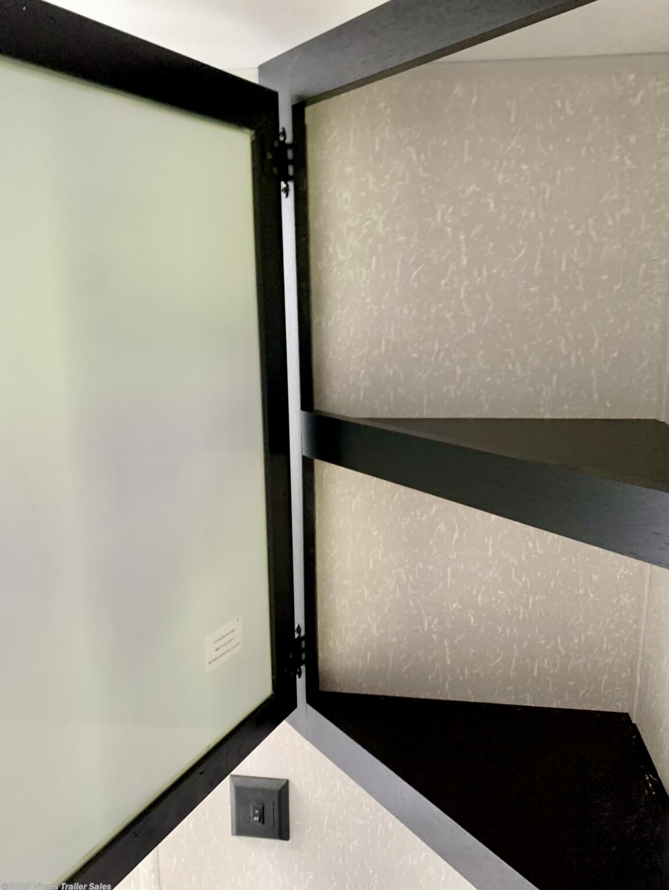 RV rental: Open cabinet with a frosted door, dark shelves, and an electrical switch. Ideal for organized RV storage.. Forest River Cherokee Grey Wolf 2022