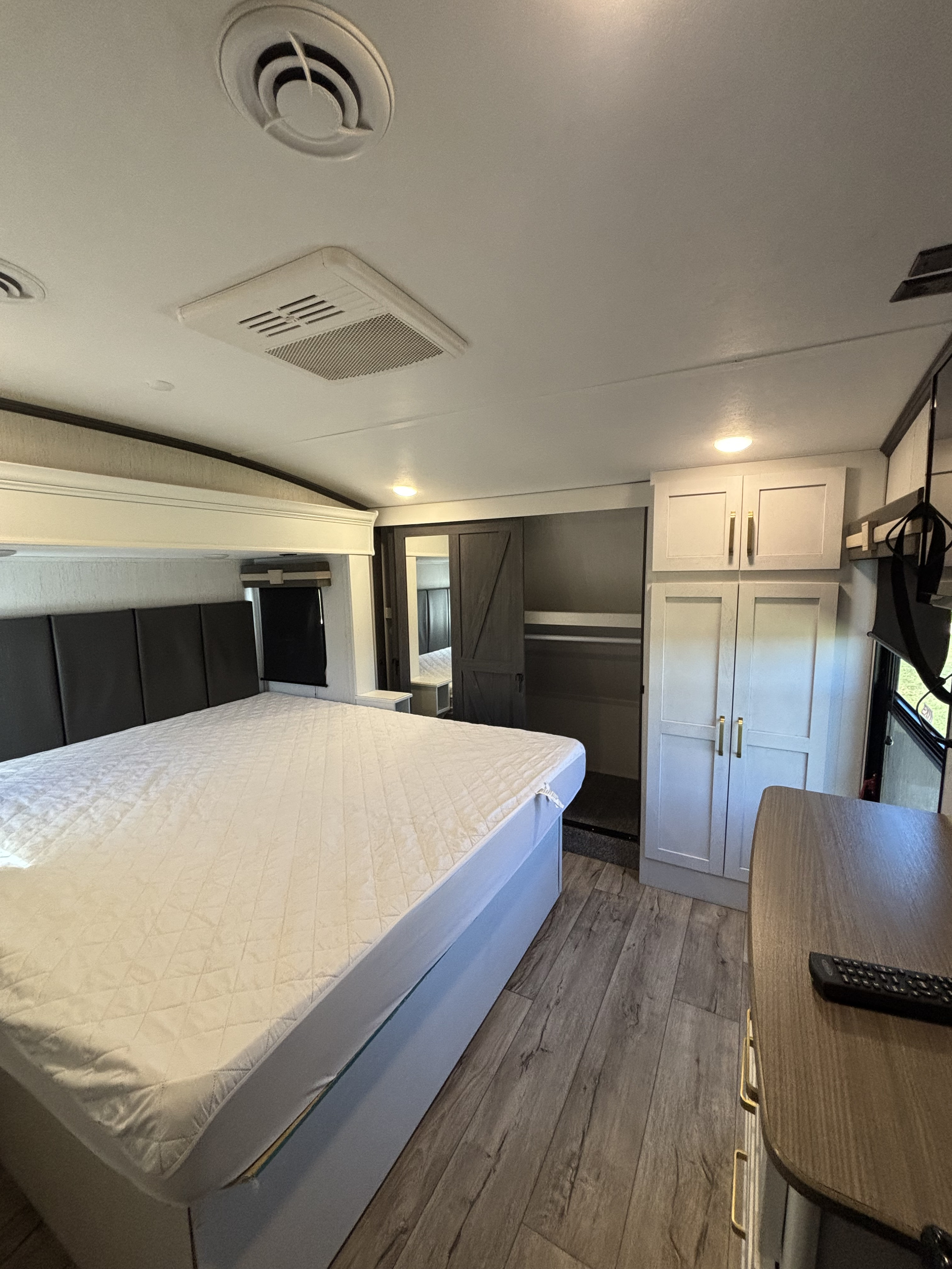 RV rental bedroom: a comfortable space featuring a large bed, padded headboard, built-in wardrobe, and light wood flooring.. Keystone Astoria 2023