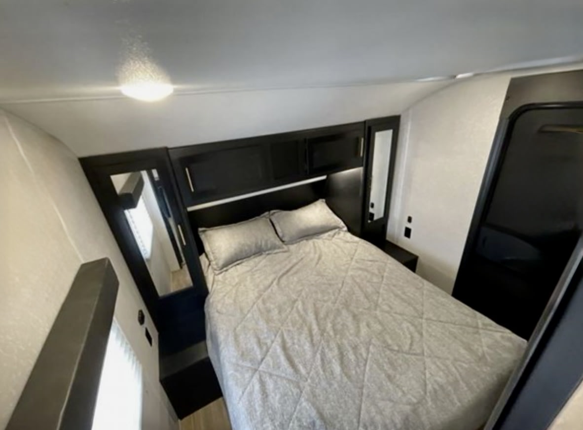 Modern RV rental bedroom. Features a comfy bed, overhead cabinets, and mirrored wardrobes. Ideal for a cozy travel stay.. Forest River Cherokee 2022