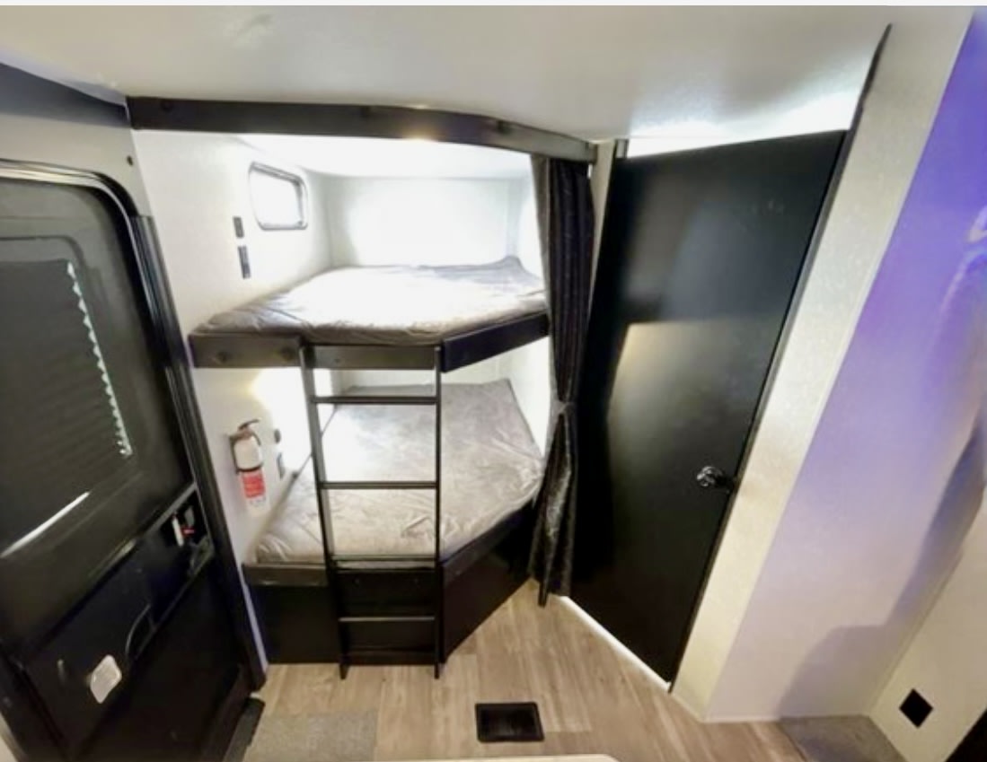 Inside an RV rental, this cozy bunkhouse features sleeping for two, a ladder, and a safety extinguisher. Perfect for family adventures.. Forest River Cherokee 2022