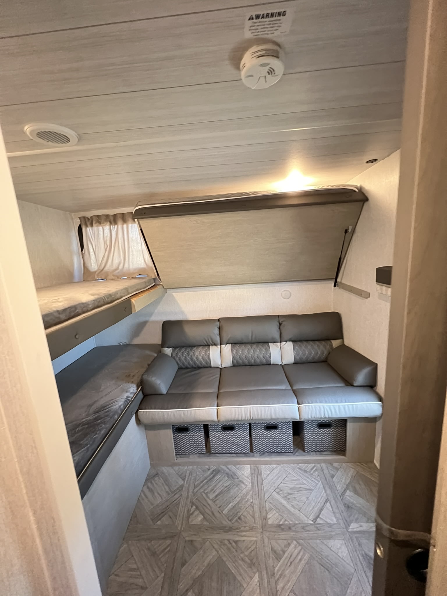 Modern RV rental interior with cozy bunk beds, a versatile sofa featuring a lift-up bed, and under-seat storage bins.. Forest River Wildwood X-Lite Platinum 2024