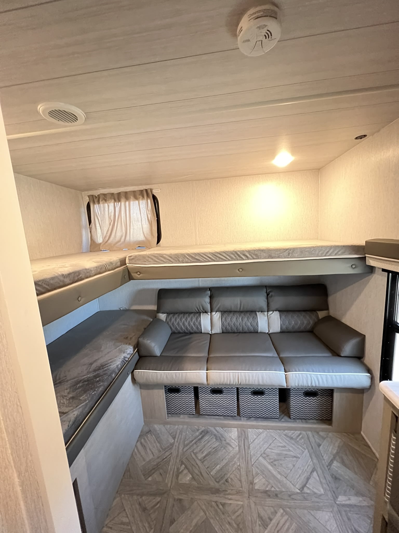 Cozy RV rental interior with bunk beds, a gray sofa, & storage bins. Ideal for family adventures and comfortable living.. Forest River Wildwood X-Lite Platinum 2024