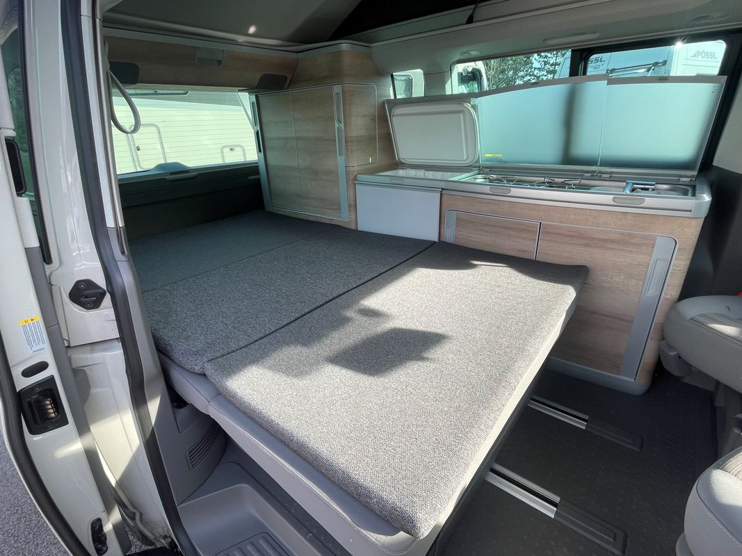 This RV rental camper van features a functional interior with a multi-segment bed, compact kitchen (stove, sink, fridge), and cabinets.. Volkswagen California Coast T6 2024