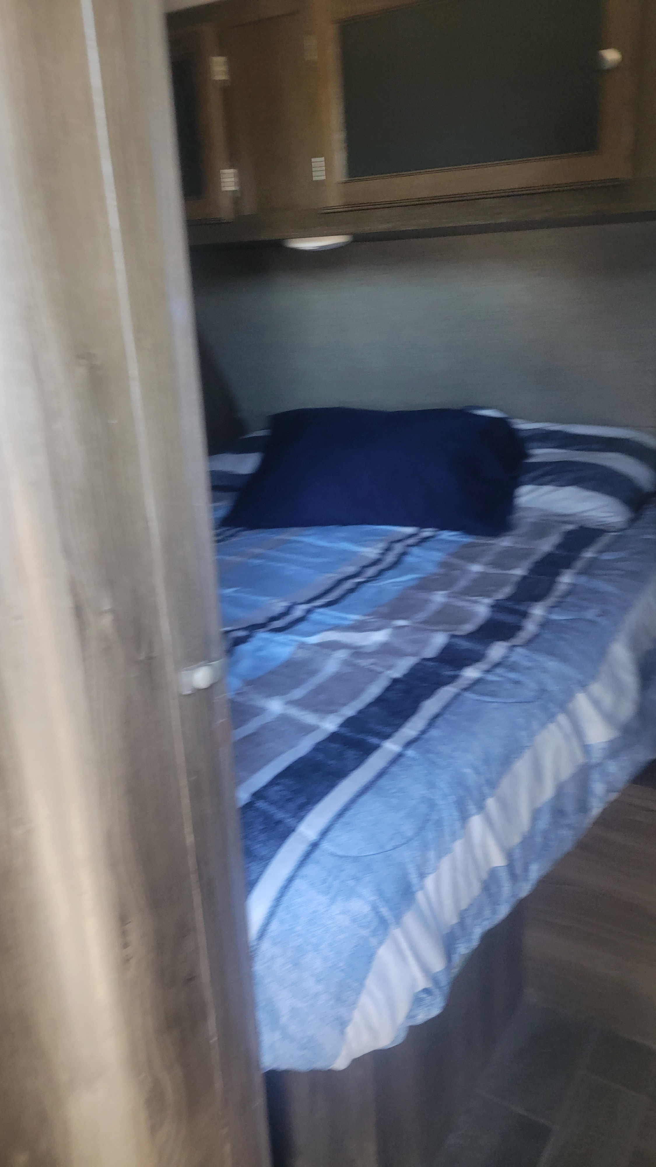 RV rental bedroom with blue striped bed, dark pillow, and wood cabinets visible.. Keystone RV Bullet Ultra Lite 2018