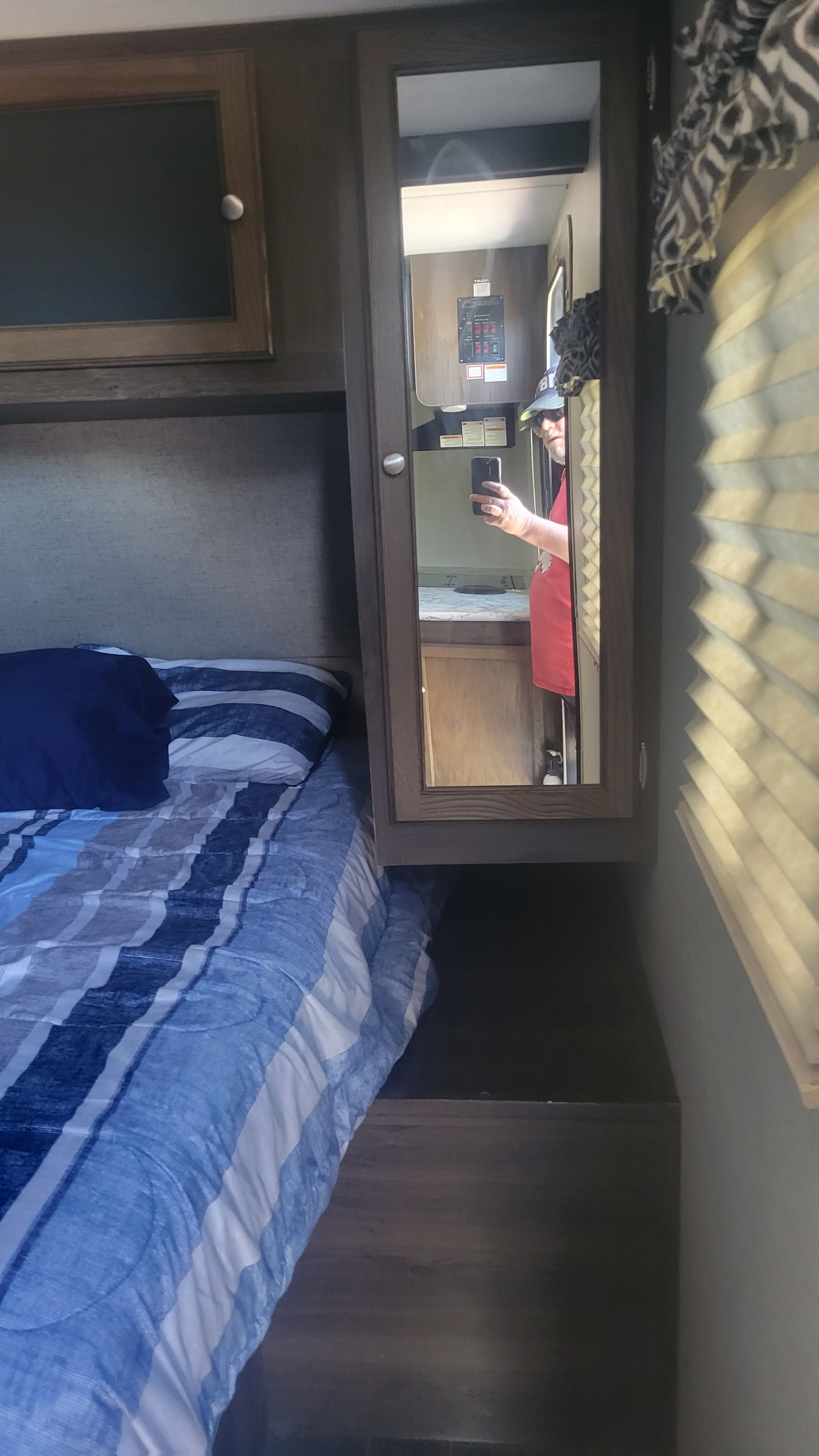 Cozy RV rental bedroom with blue striped bedding, a cabinet, and a mirror reflecting the photographer.. Keystone RV Bullet Ultra Lite 2018