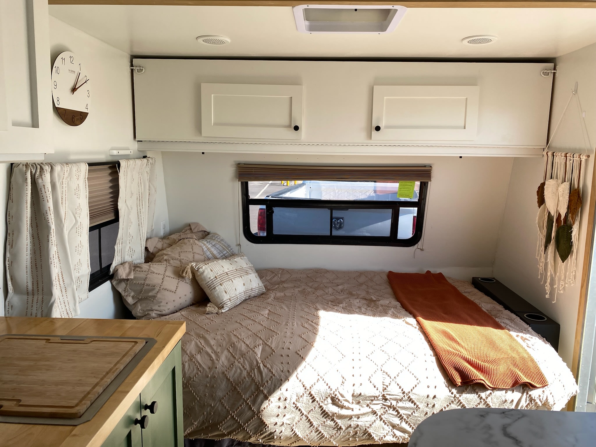 Cozy RV rental bedroom featuring a comfortable bed with pillows, overhead cabinets, windows, and bright sunlight.. Fleetwood Mallard 23P 2024