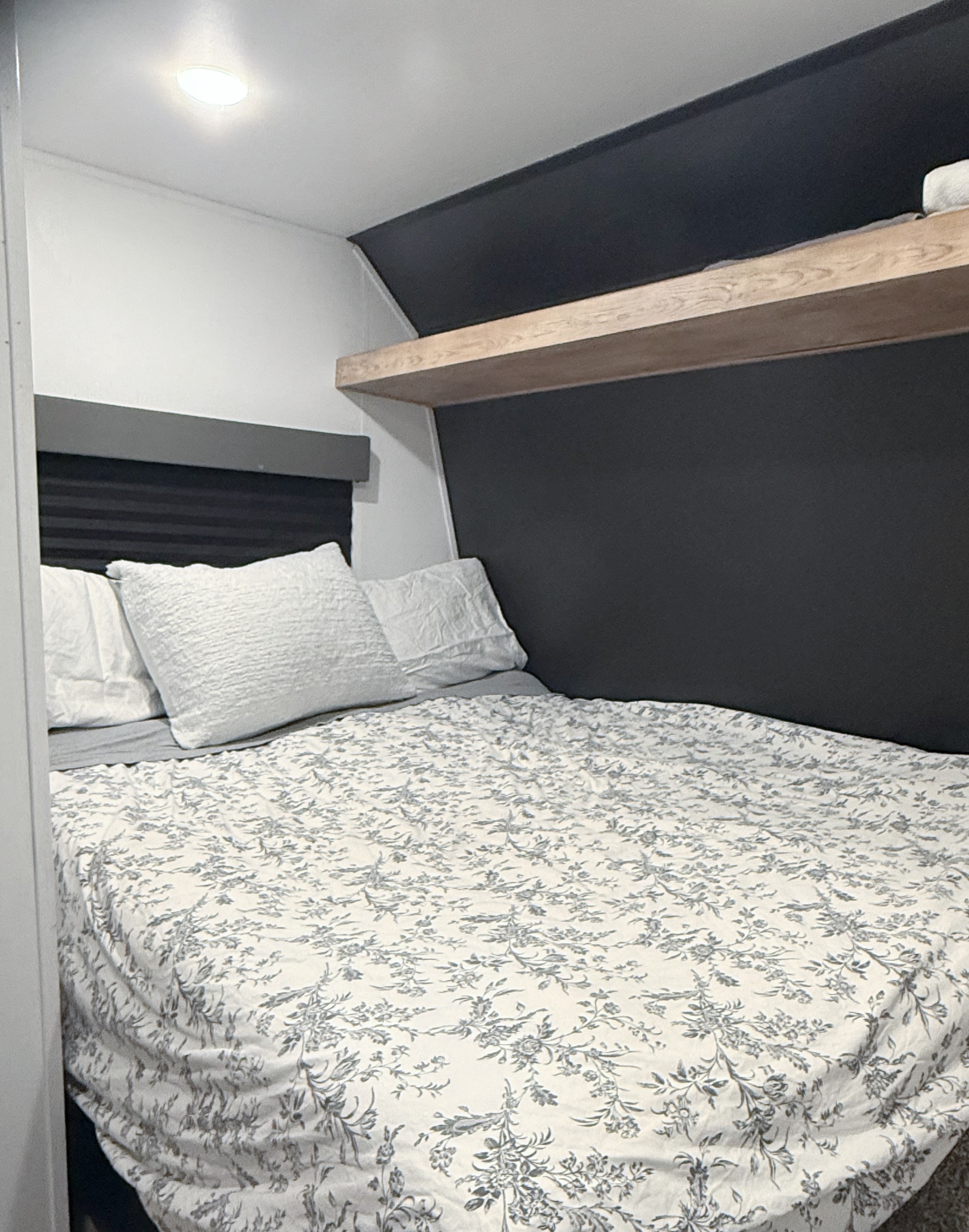 Inviting RV rental bedroom: patterned bed, white/gray decor, built-in shelf, and dark headboard wall for your trips.. Forest River Wildwood FSX 2022