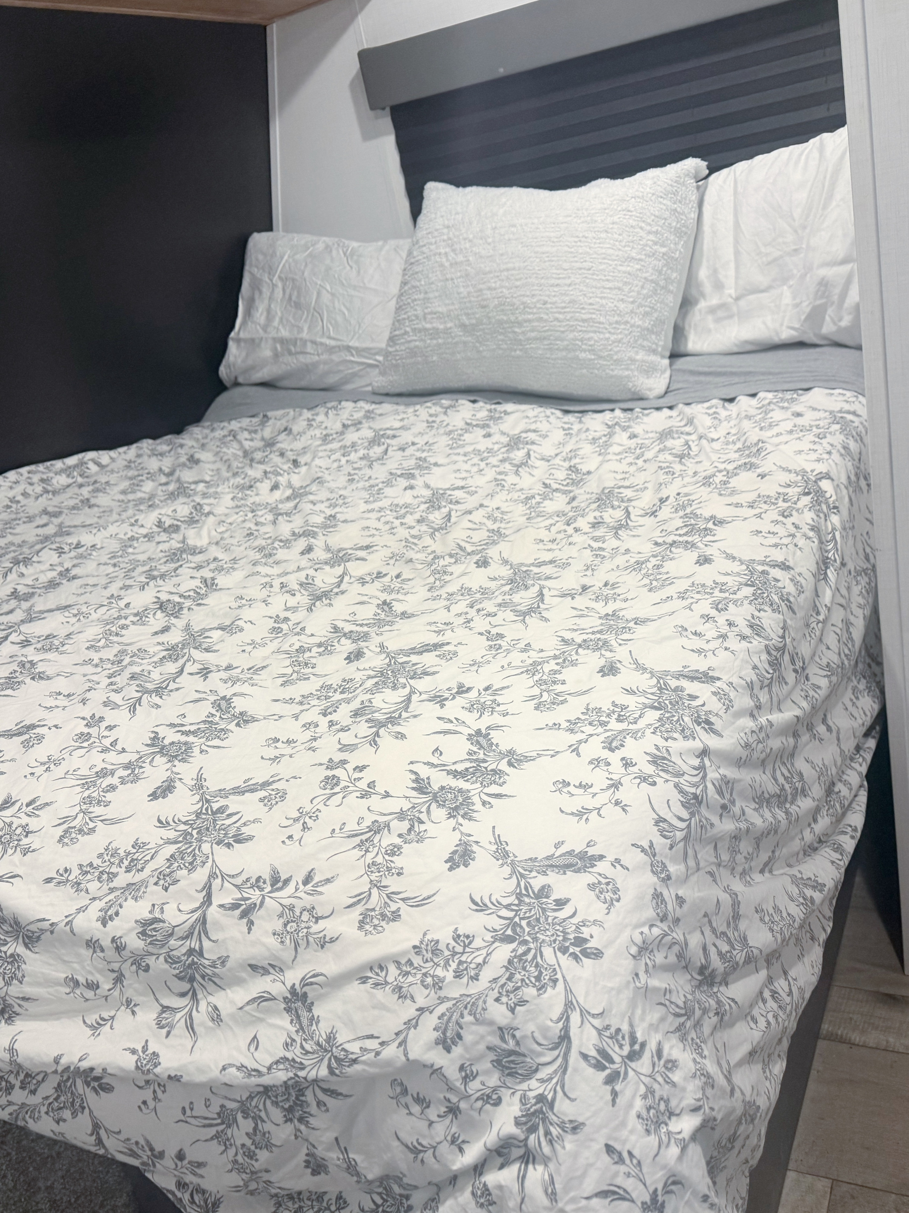 RV rental bedroom: A neatly made bed with white and gray floral bedding and white pillows, against dark and light walls.. Forest River Wildwood FSX 2022