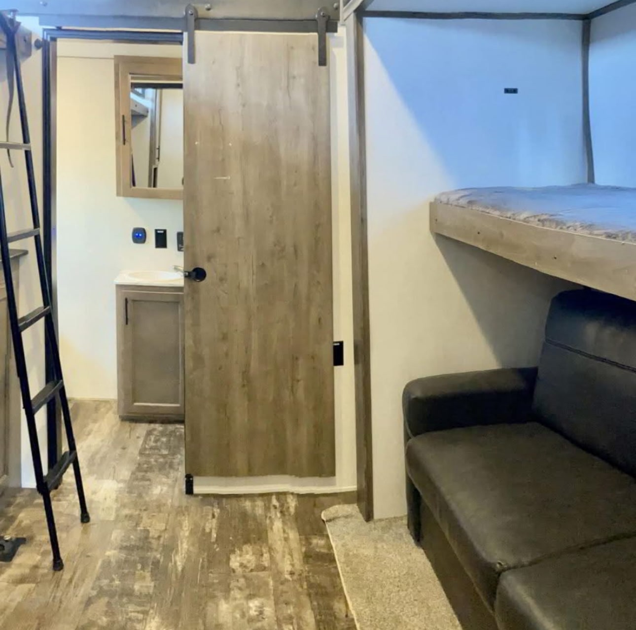 This RV rental interior showcases a bathroom with a sliding barn door, a bunk bed above a sofa, and a ladder.. Forest River Sabre 2021