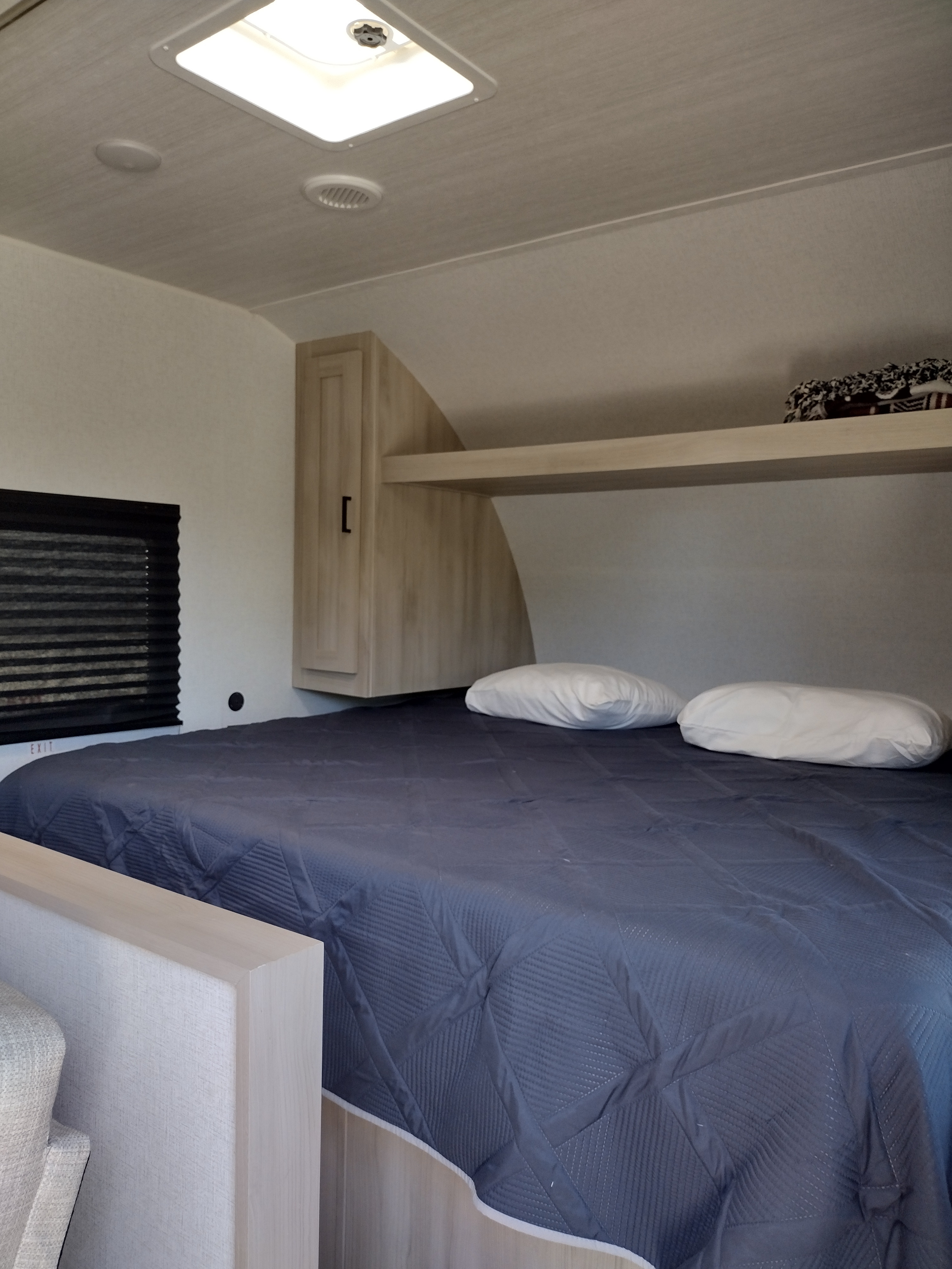 Cozy RV rental bedroom with a dark blue bed, pillows, overhead storage, and a window for comfortable travel.. East to West Della Terra LE 2024