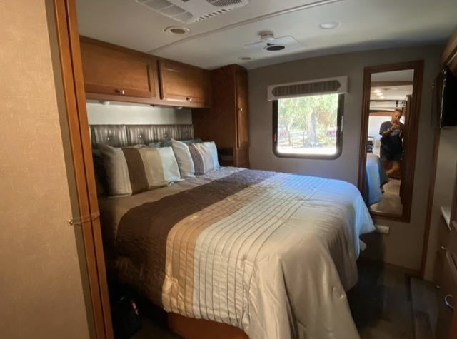Spacious RV rental bedroom featuring a comfortable bed, overhead cabinets, window, and ceiling fan.. Winnebago Vista LX 2019