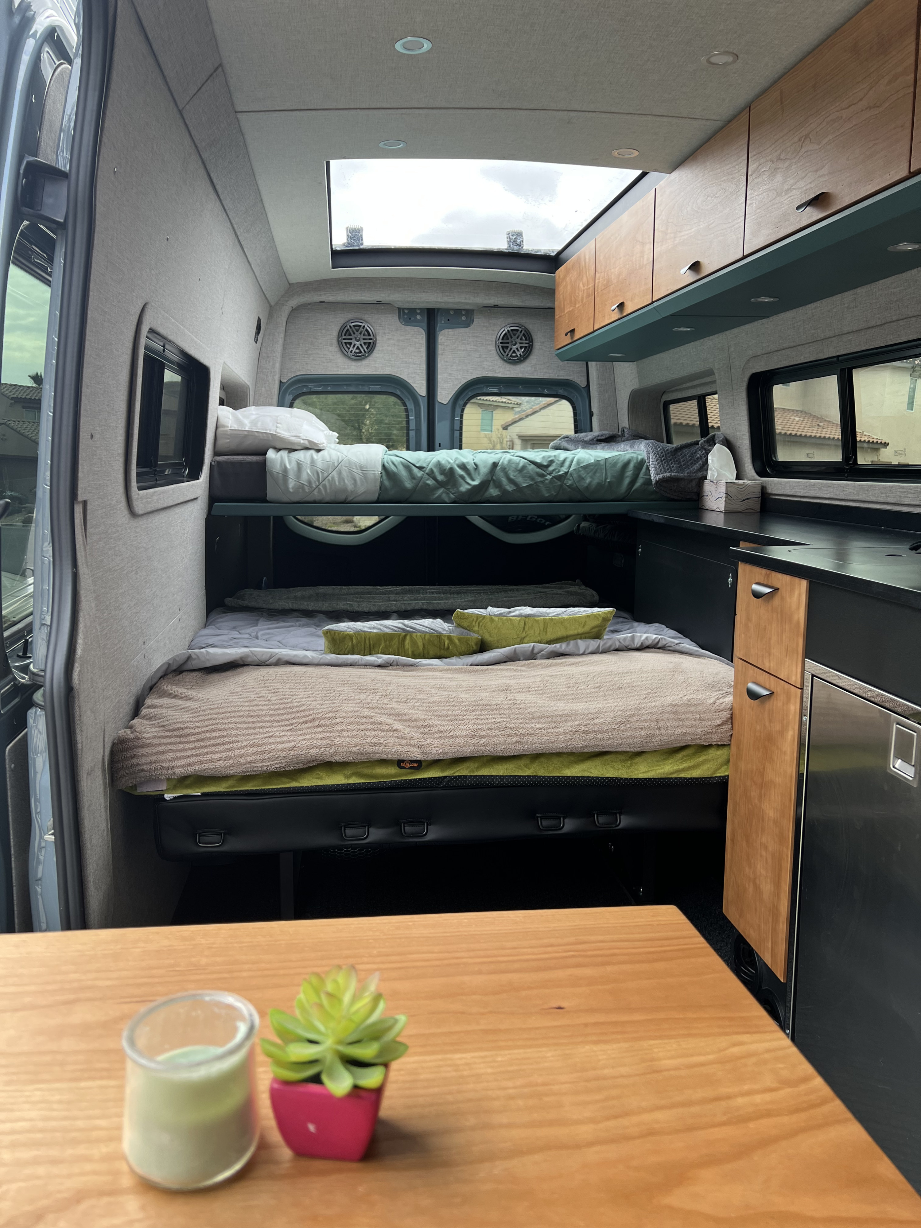 RV rental interior view: bunk beds, lower bed, compact kitchen with fridge/cabinets, and bright skylight above.. Off Highway Van Off Highway Van Class B 2024