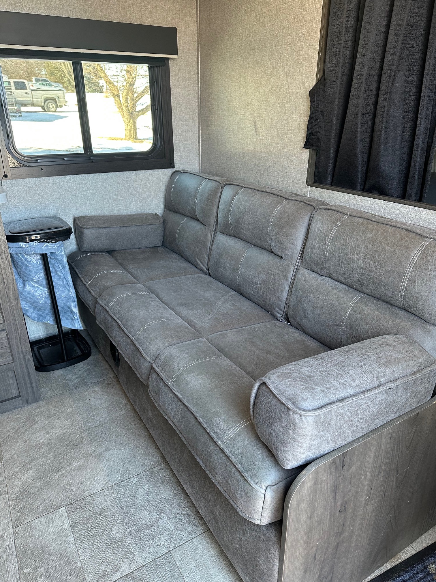 Modern RV rental: a spacious interior with a long, comfy gray sofa & a beautiful snowy winter view from the window.. Jayco Jay Flight SLX 2020