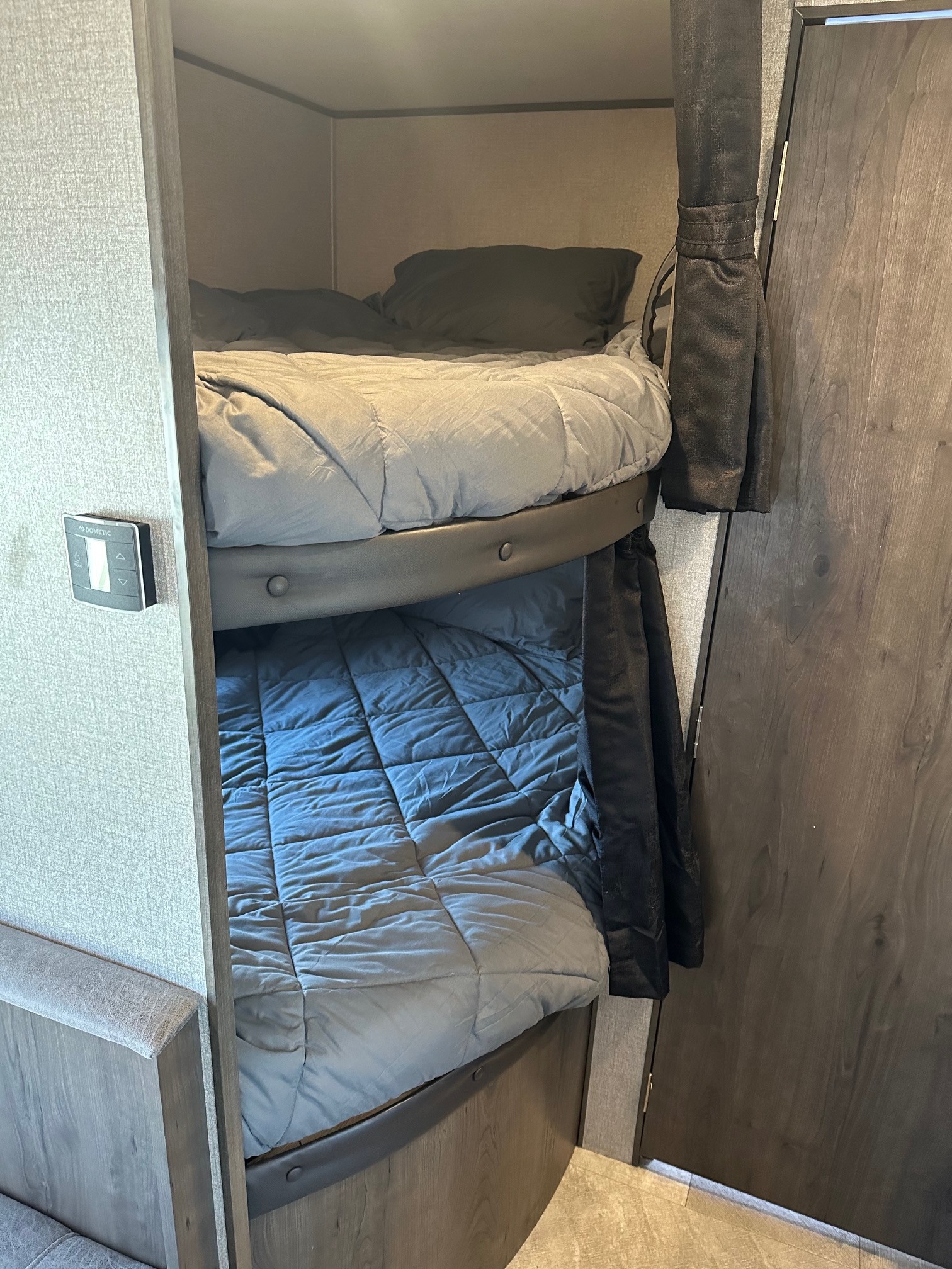 Inside an RV rental: two cozy bunk beds with bedding, featuring a Dometic control panel and privacy curtain for comfort.. Jayco Jay Flight SLX 2020