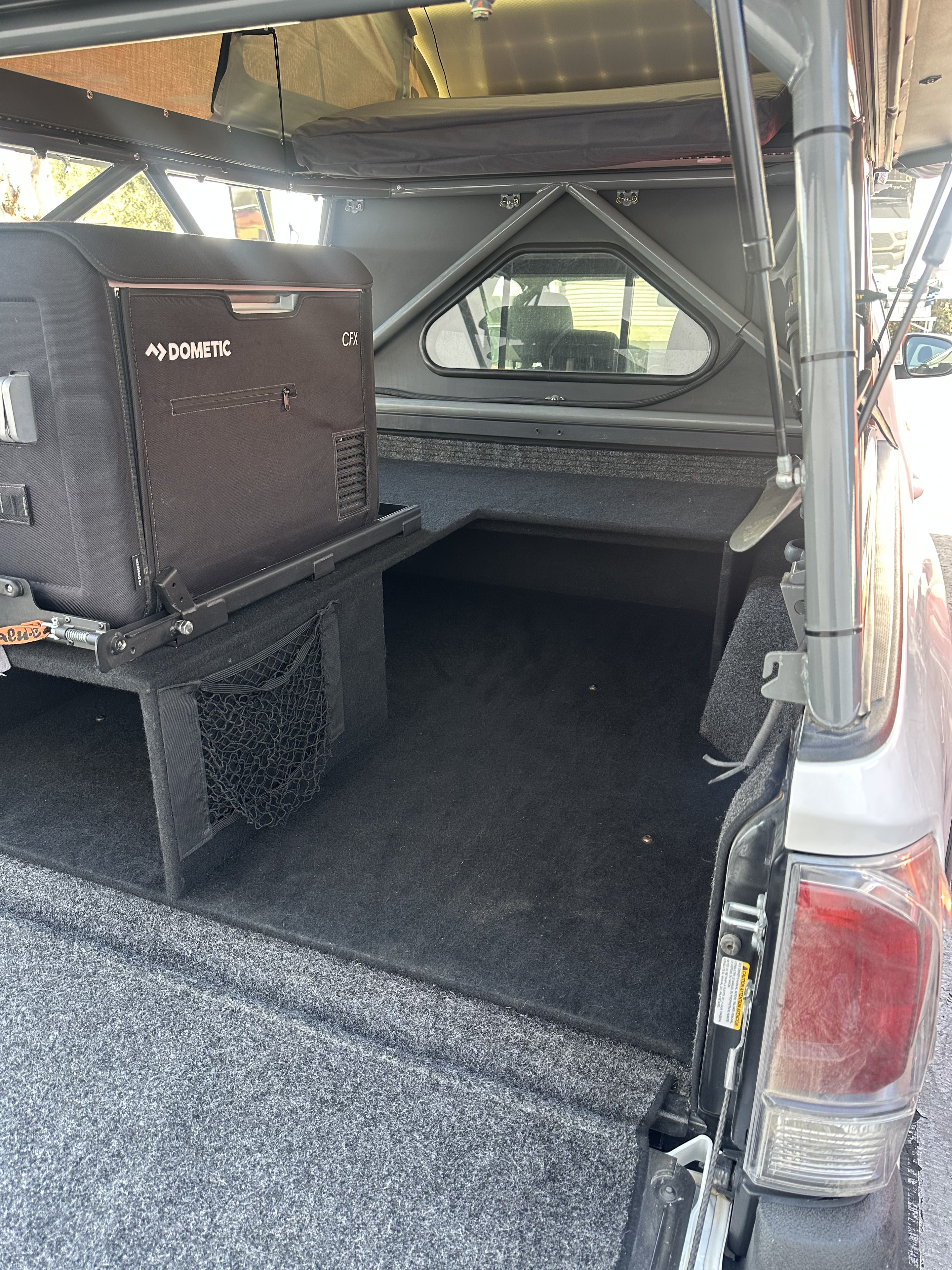 RV rental interior: Dometic fridge on slider, custom truck bed storage, and a sturdy pop-top camper shell.. 2023