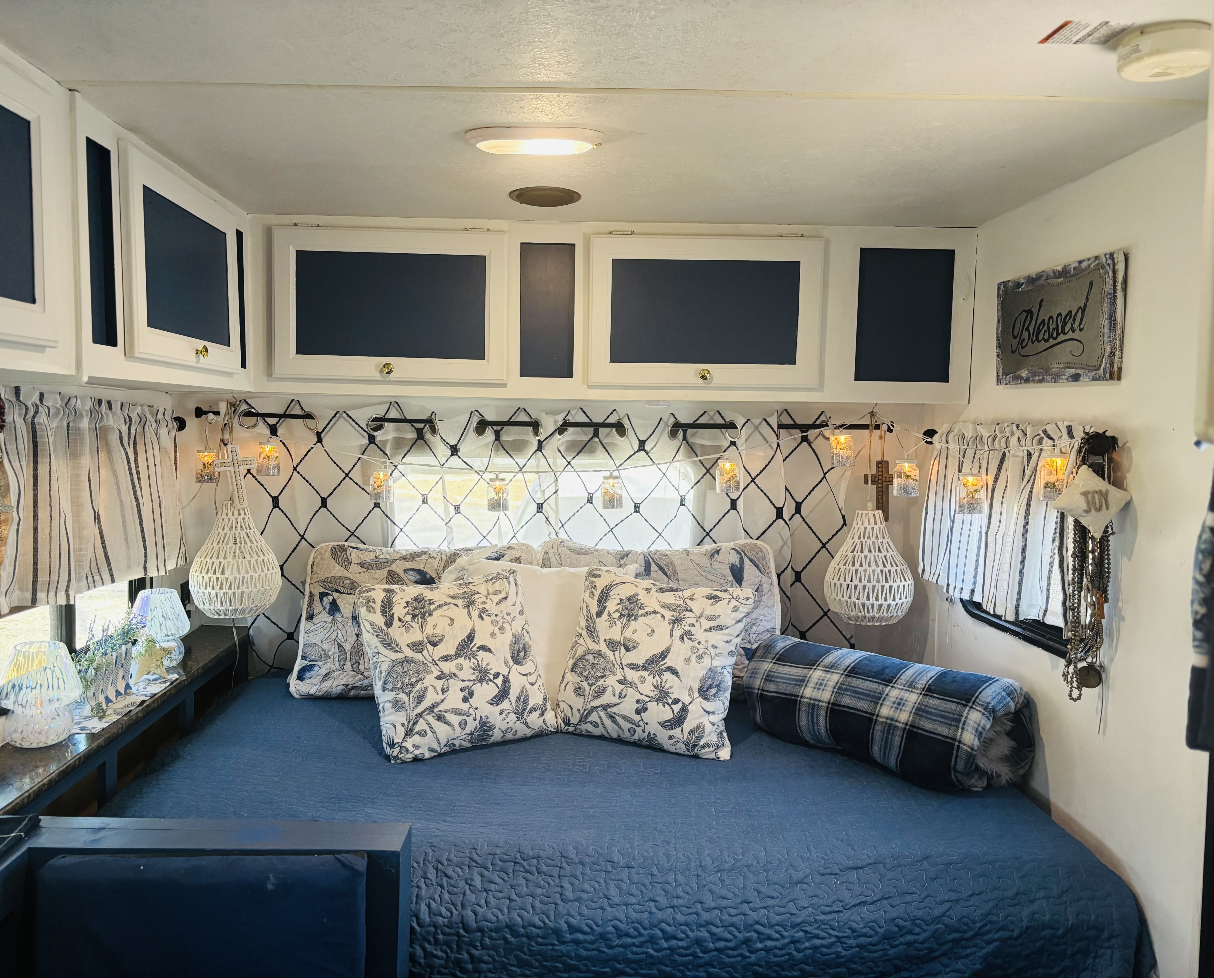 Cozy RV rental bedroom with a blue quilted bedspread, floral pillows, overhead cabinets, and charming string lights.. Clipper Clipper Trailer 2016