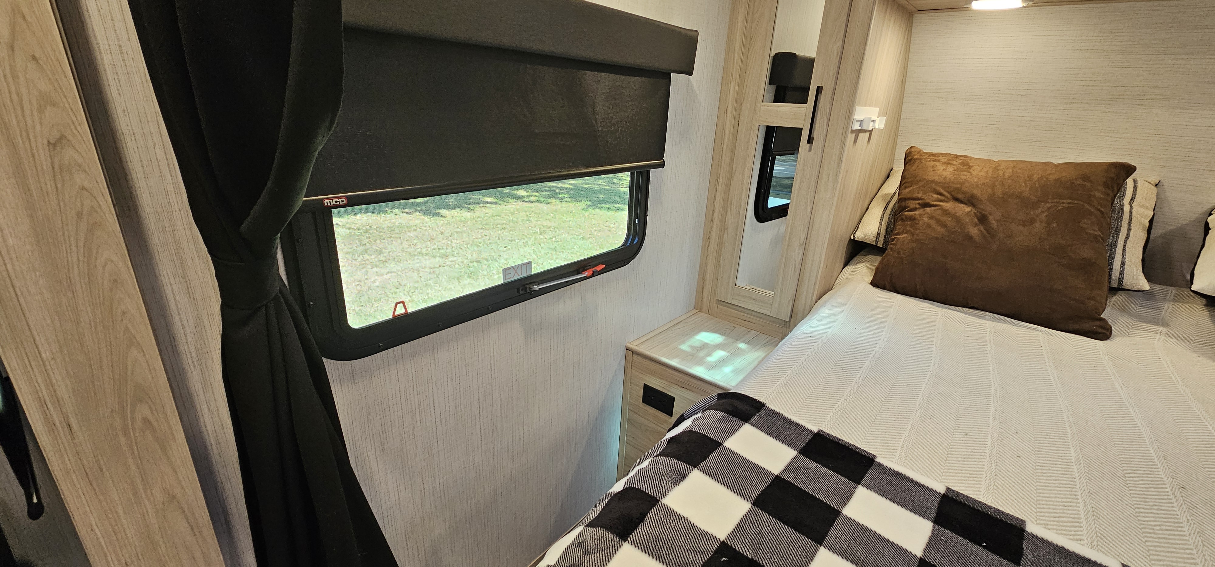 RV rental bedroom: cozy bed with plaid blanket, window with 'EXIT' label, and wood interior.. Heartland RVs Sundance Ultra Lite 2022